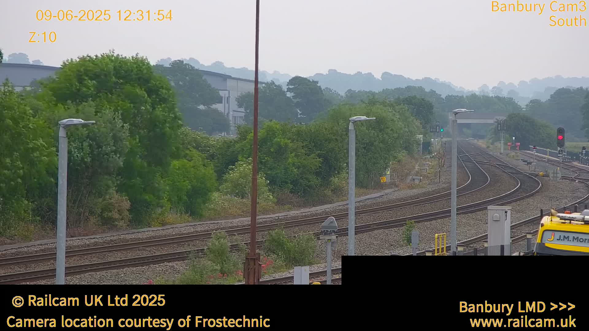 A hazy view of a railway yard with multiple tracks curving through a landscape of lush green trees and foliage under an overcast sky.