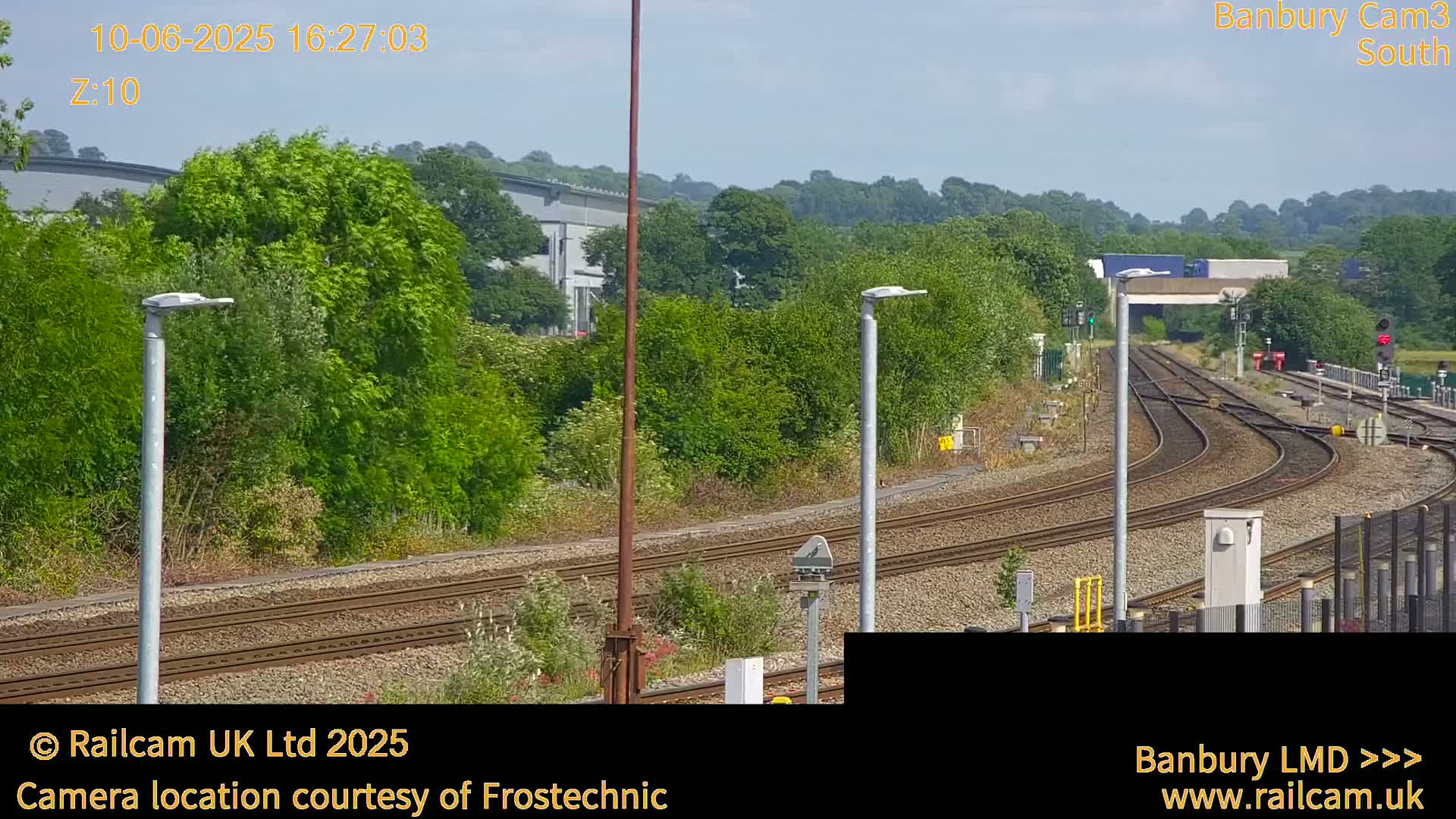 A sunny view of a railway yard with several sets of tracks curving through a landscape of green trees and bushes.