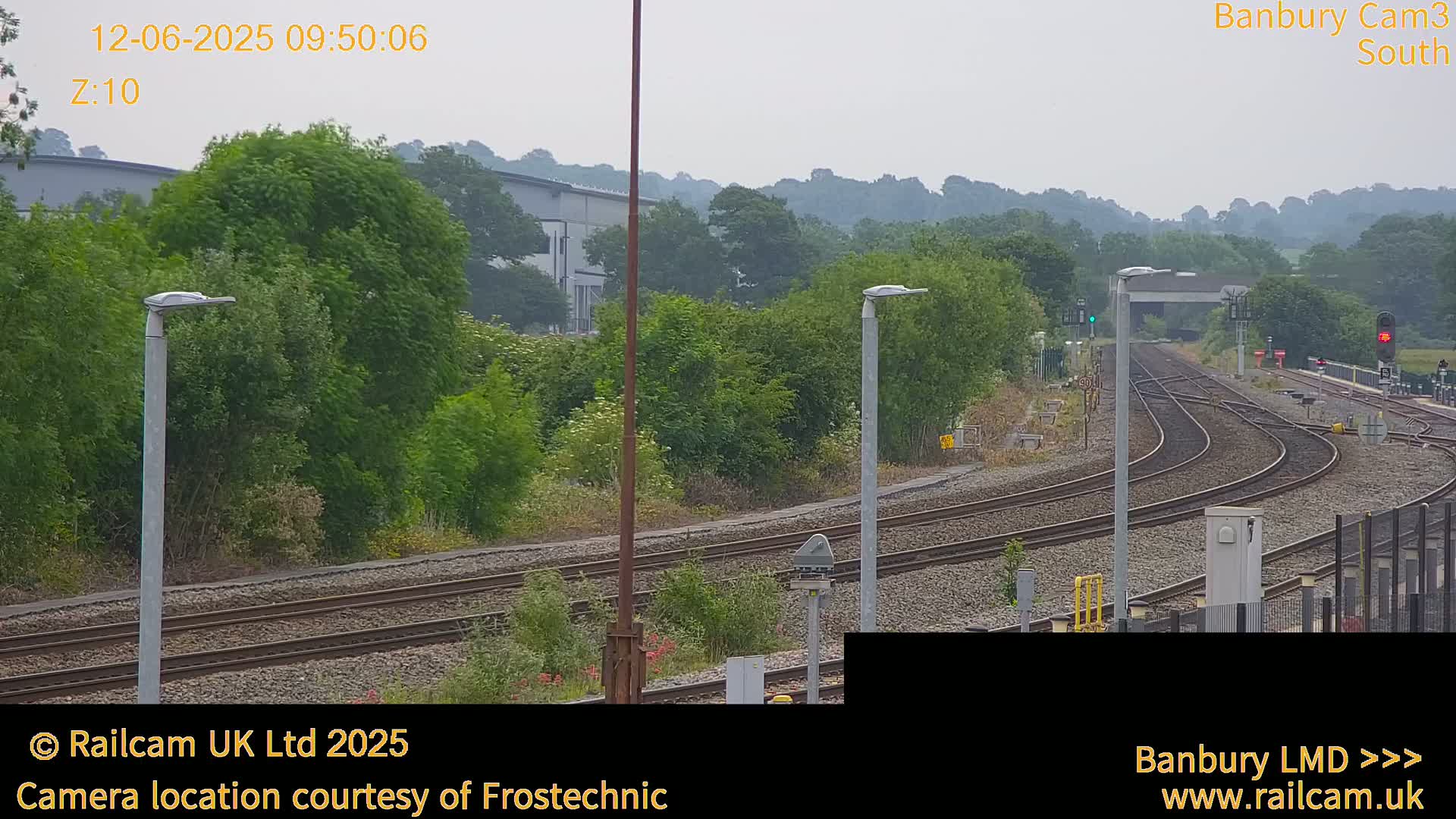 A view of several train tracks curving through a landscape of green trees and shrubs under an overcast sky.