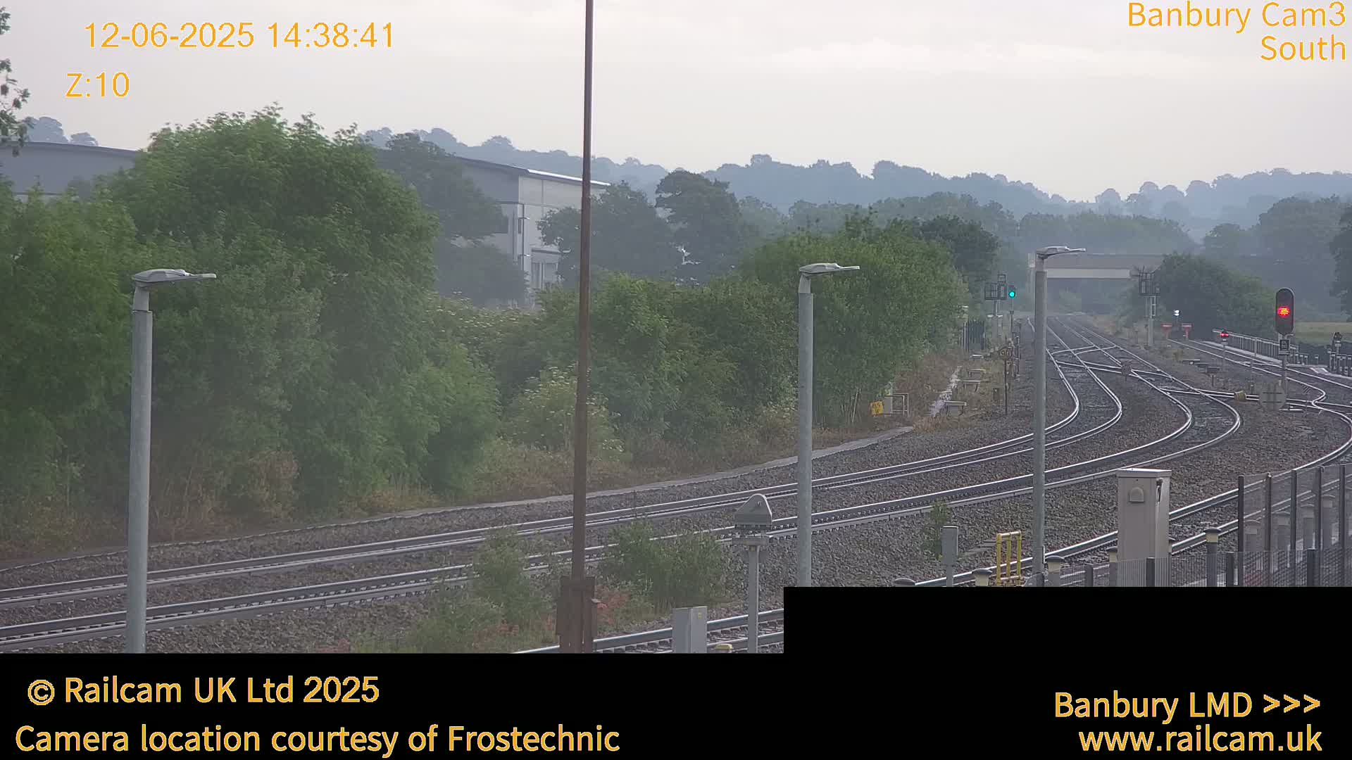 A hazy view of multiple train tracks curving through a landscape of green vegetation and distant hills under a muted sky.