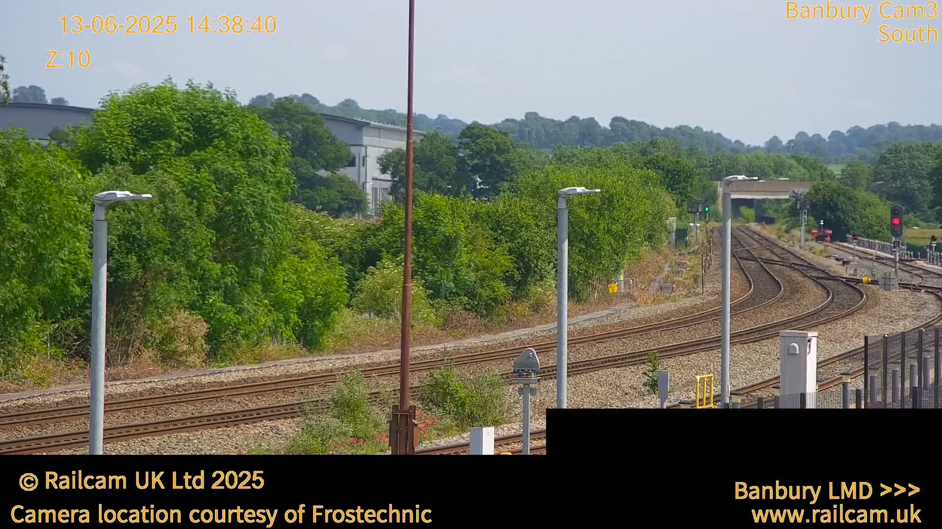 Under a sunny sky, a view of several train tracks curves through a landscape of green trees and vegetation.