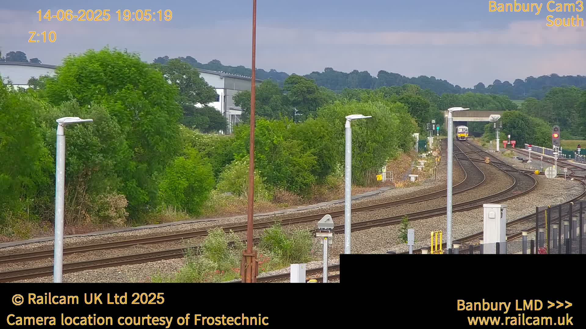 A train is traveling on a railway track surrounded by green vegetation under a partly cloudy sky.