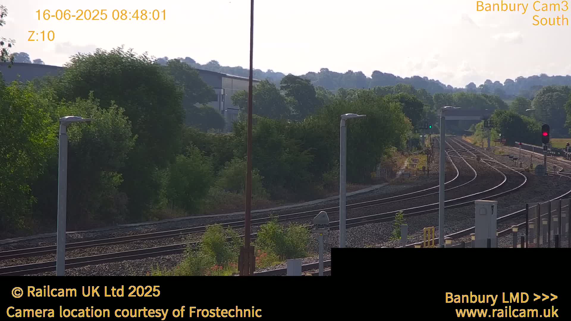 A view of train tracks curving through a landscape of green trees and shrubs under a hazy sky.