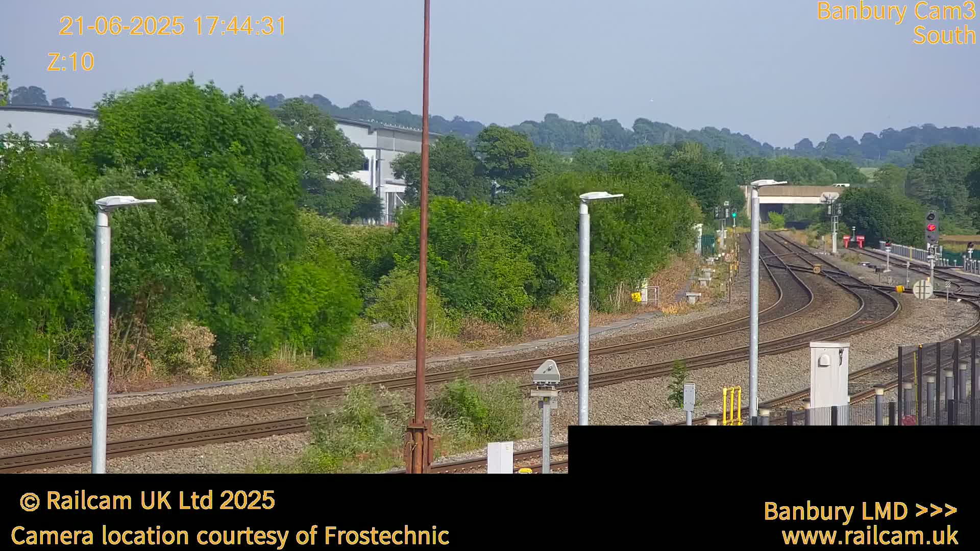 A sunny view of railway tracks curving through a landscape of lush green vegetation and trees, under a clear sky.
