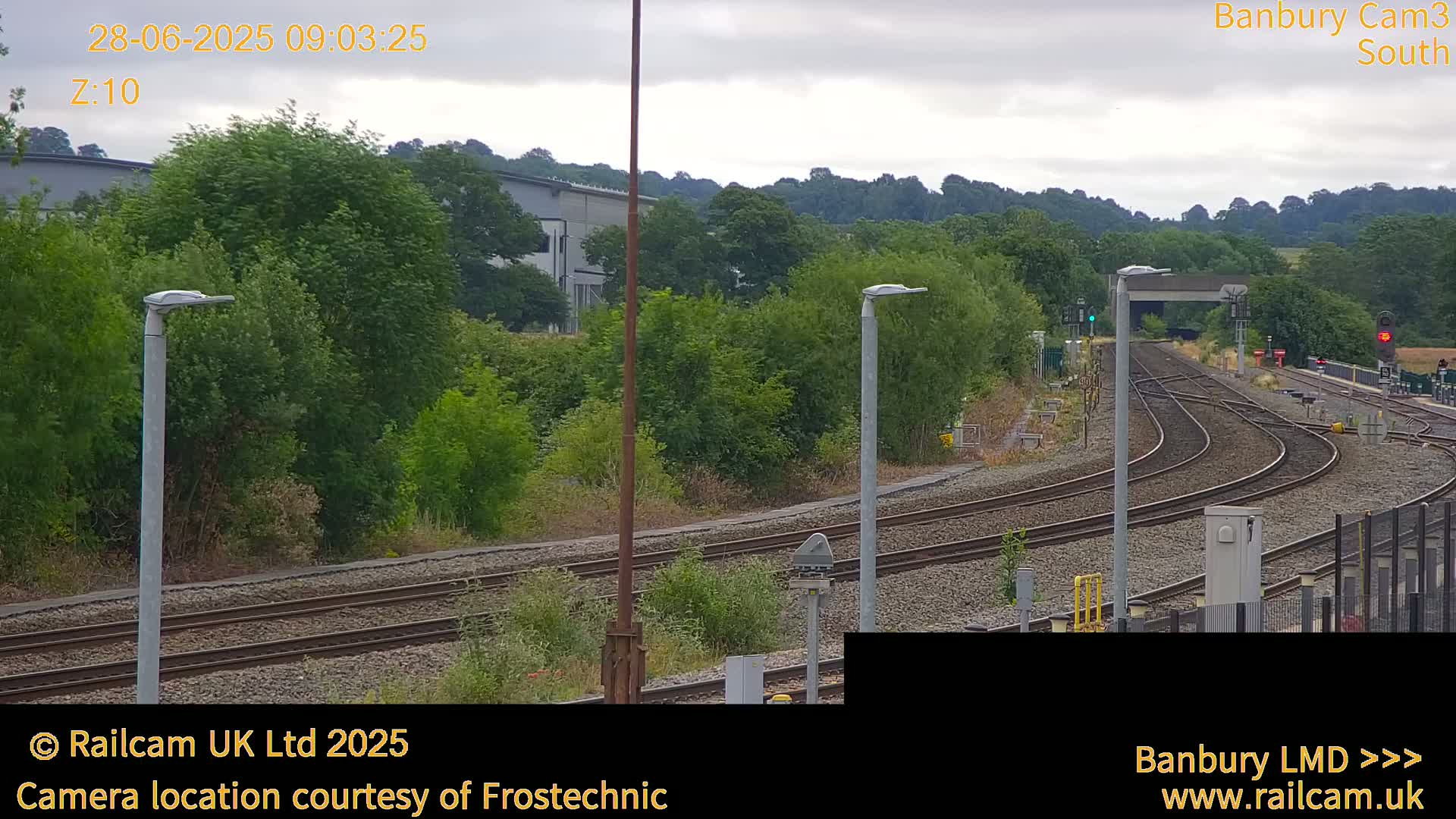 A view of curving train tracks surrounded by lush green vegetation under an overcast sky.