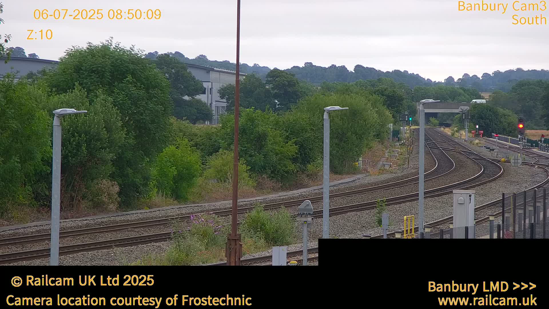 A view of a railway track curving through a landscape of green trees and shrubs under an overcast sky.
