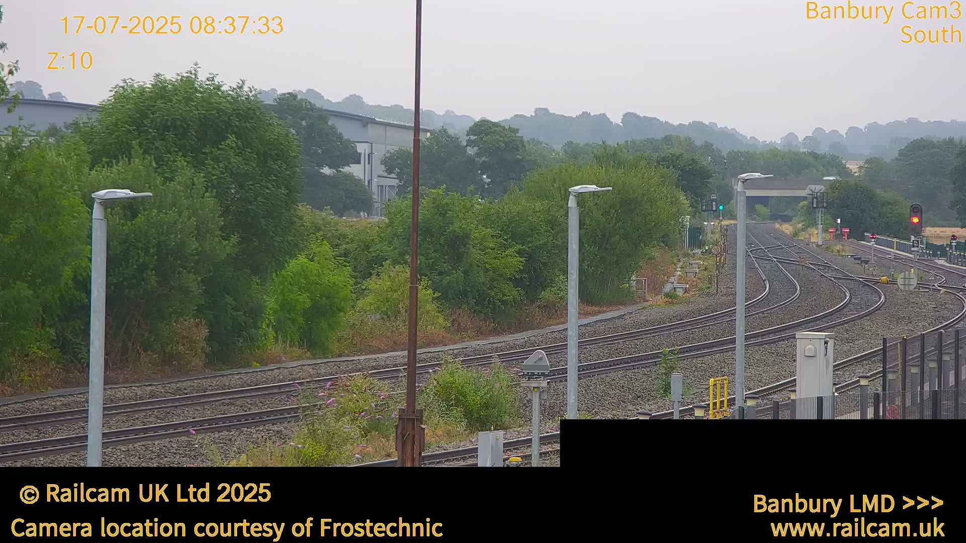 A hazy view of train tracks curving through a landscape of green trees and shrubs under an overcast sky.