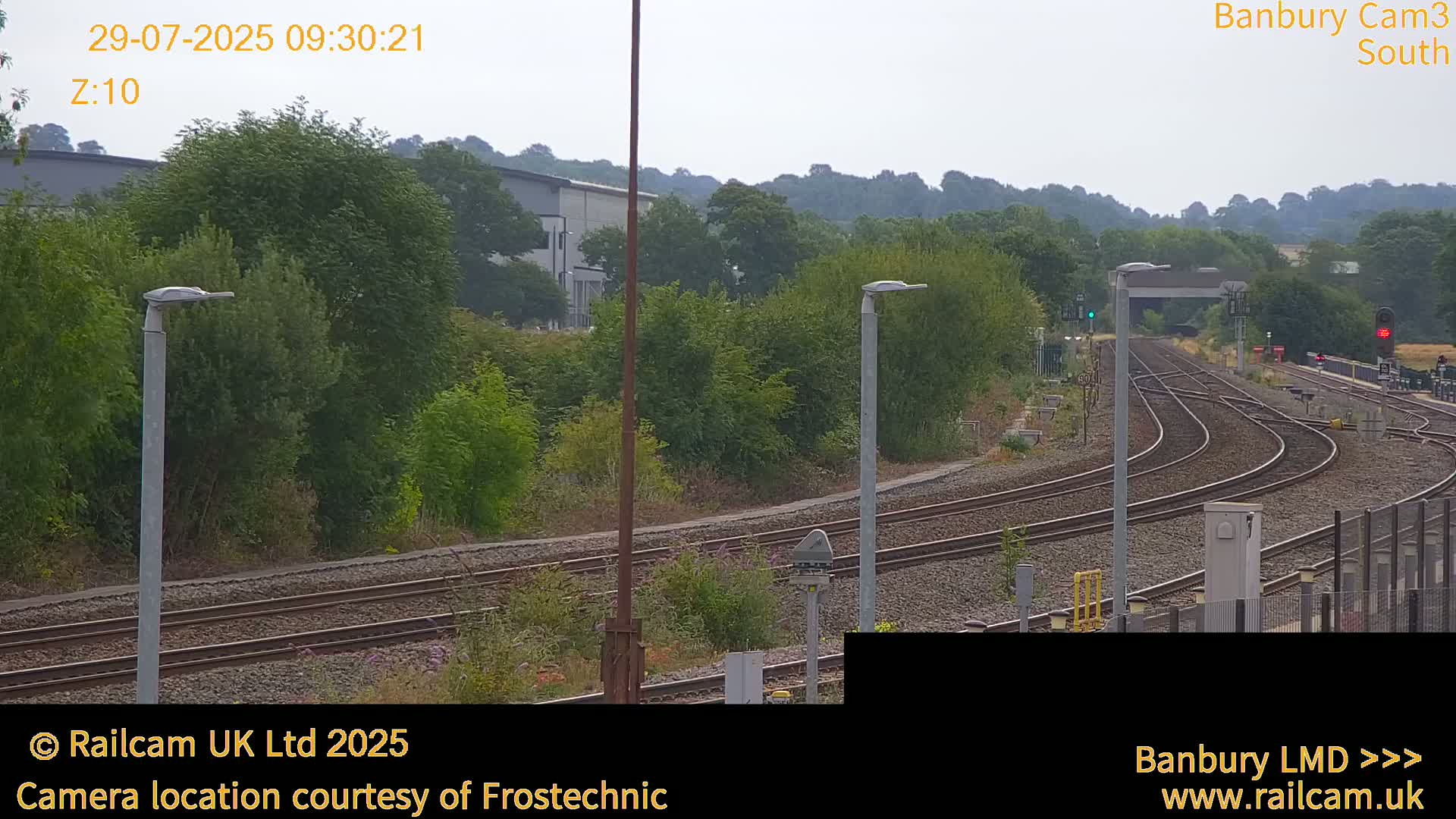 A hazy view of train tracks curving through a landscape of green trees and shrubs under an overcast sky.