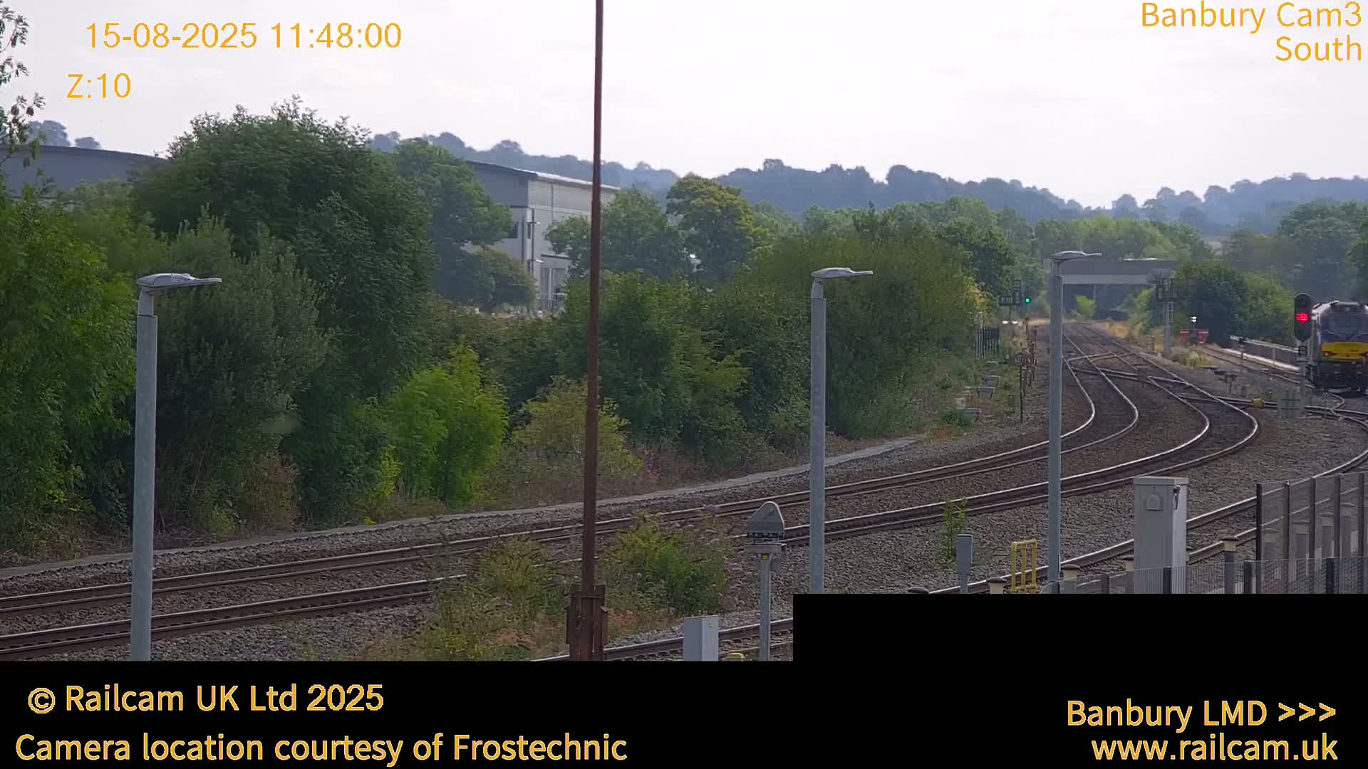 A hazy view of train tracks curving through a landscape of green trees and shrubs under an overcast sky.