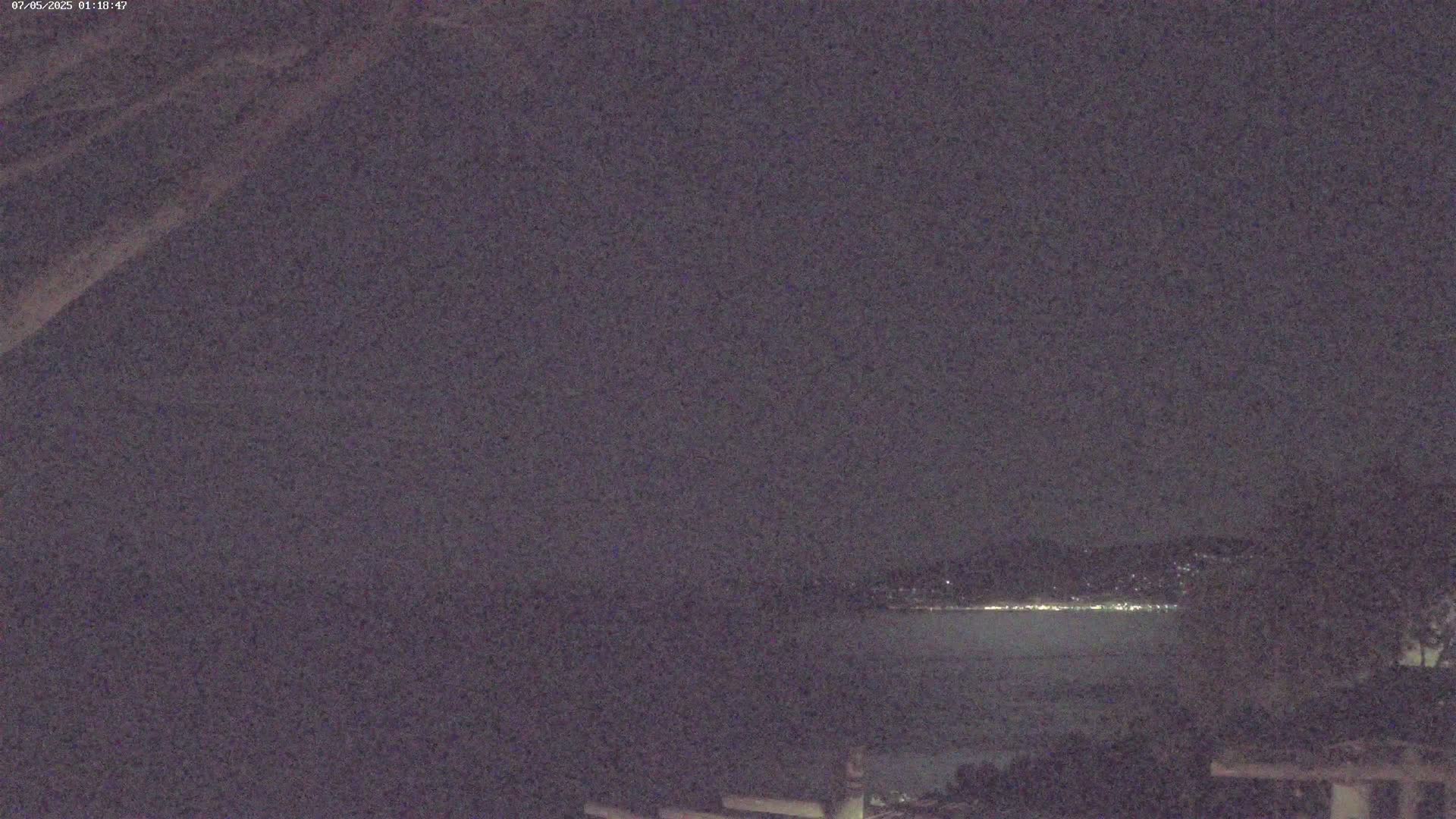 A nighttime view of a dark body of water with a distant, faintly lit shoreline under a mostly clear sky.