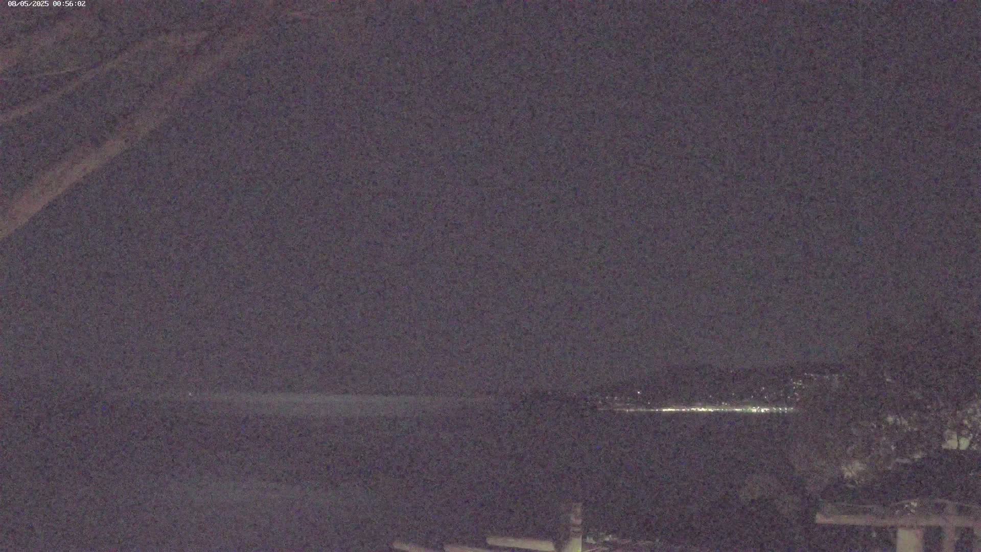 A nighttime, low-light view shows a dark body of water with a distant line of lights on the horizon.