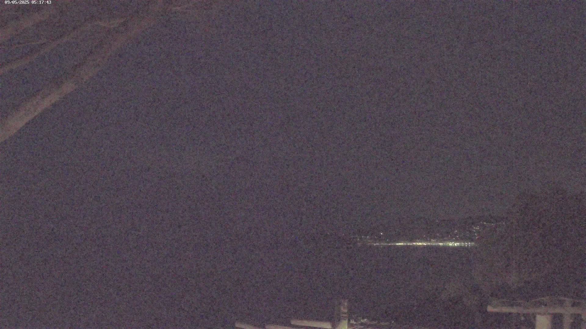 A nighttime view shows a dimly lit cityscape on the horizon across a dark body of water.
