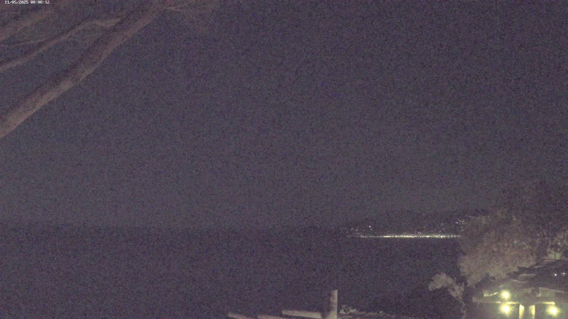 A nighttime view shows a dark body of water with a faintly lit cityscape in the distance under a clear, dark sky.