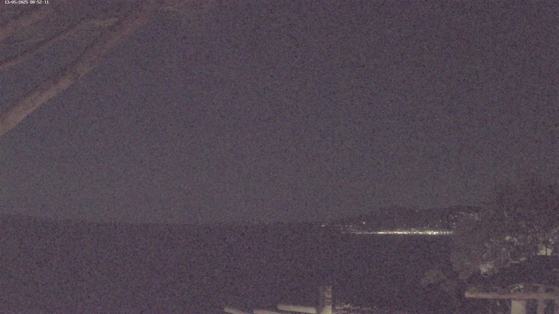 A nighttime, long-range view shows a dark body of water with a faint line of lights on the far shore under a dark, overcast sky.