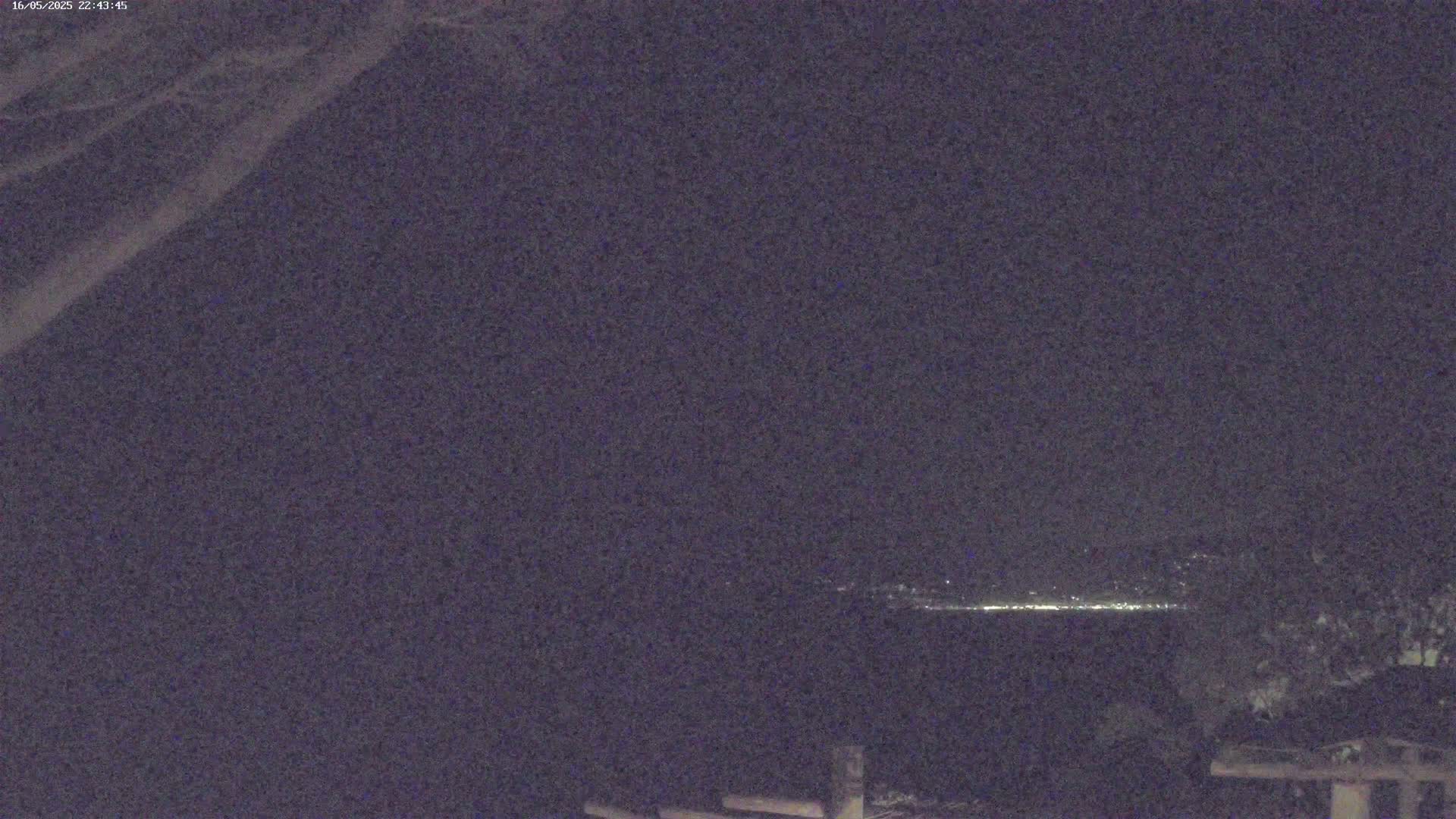 A nighttime long shot shows a distant line of lights on a dark horizon, under a mostly clear, dark sky.