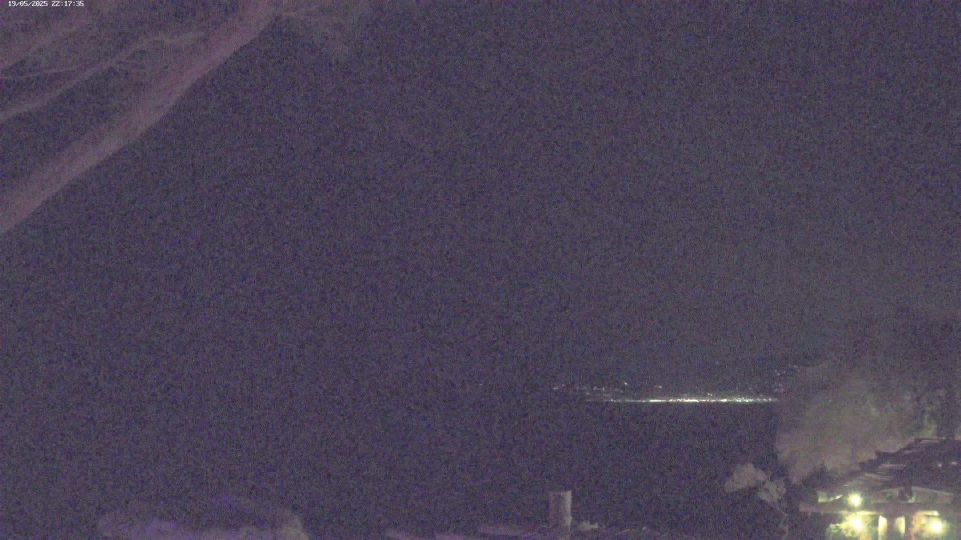 A nighttime view shows a dark body of water with distant lights on the horizon under a clear, dark sky.