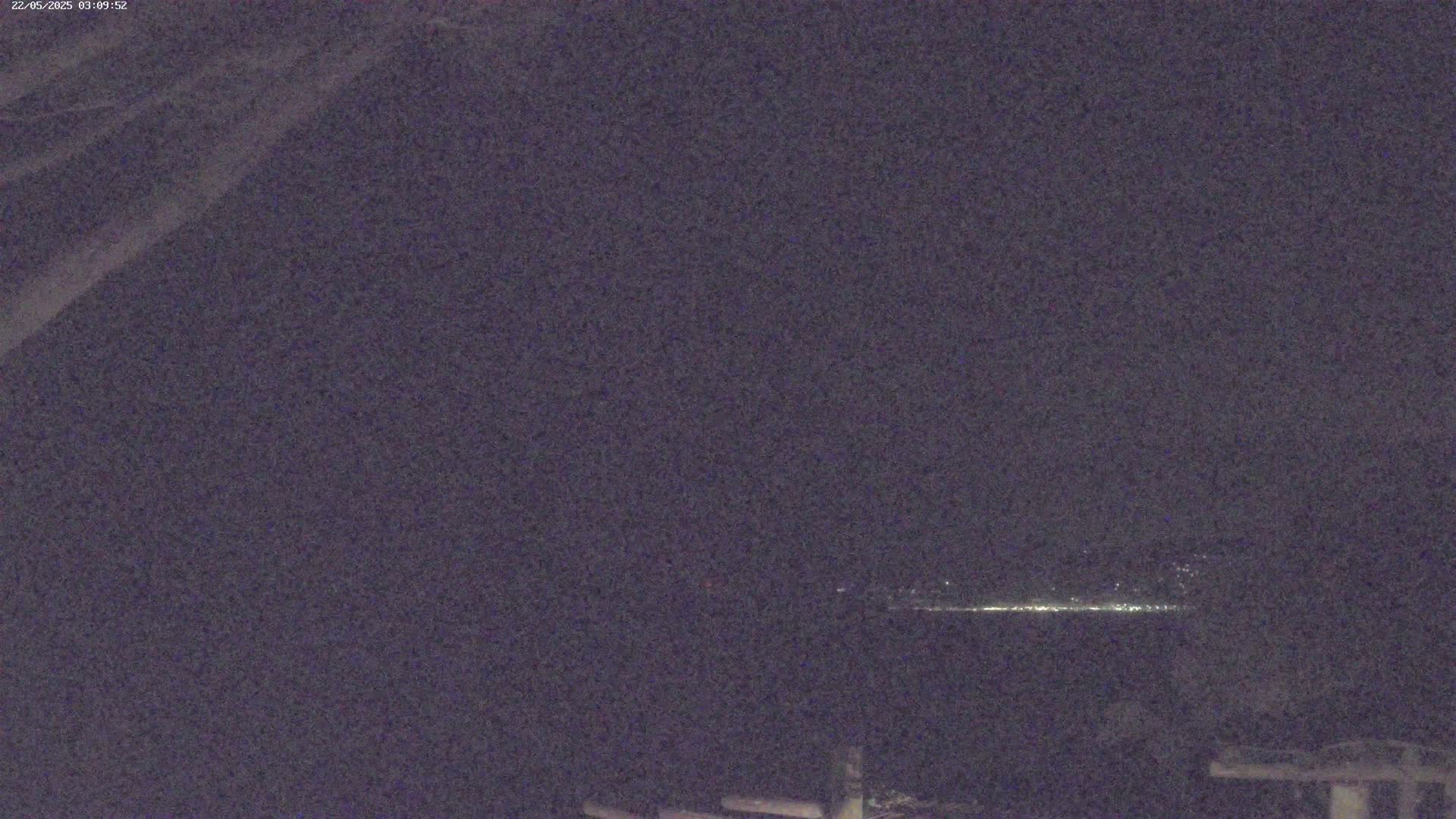 A dark, nighttime scene shows a distant line of lights on the horizon.