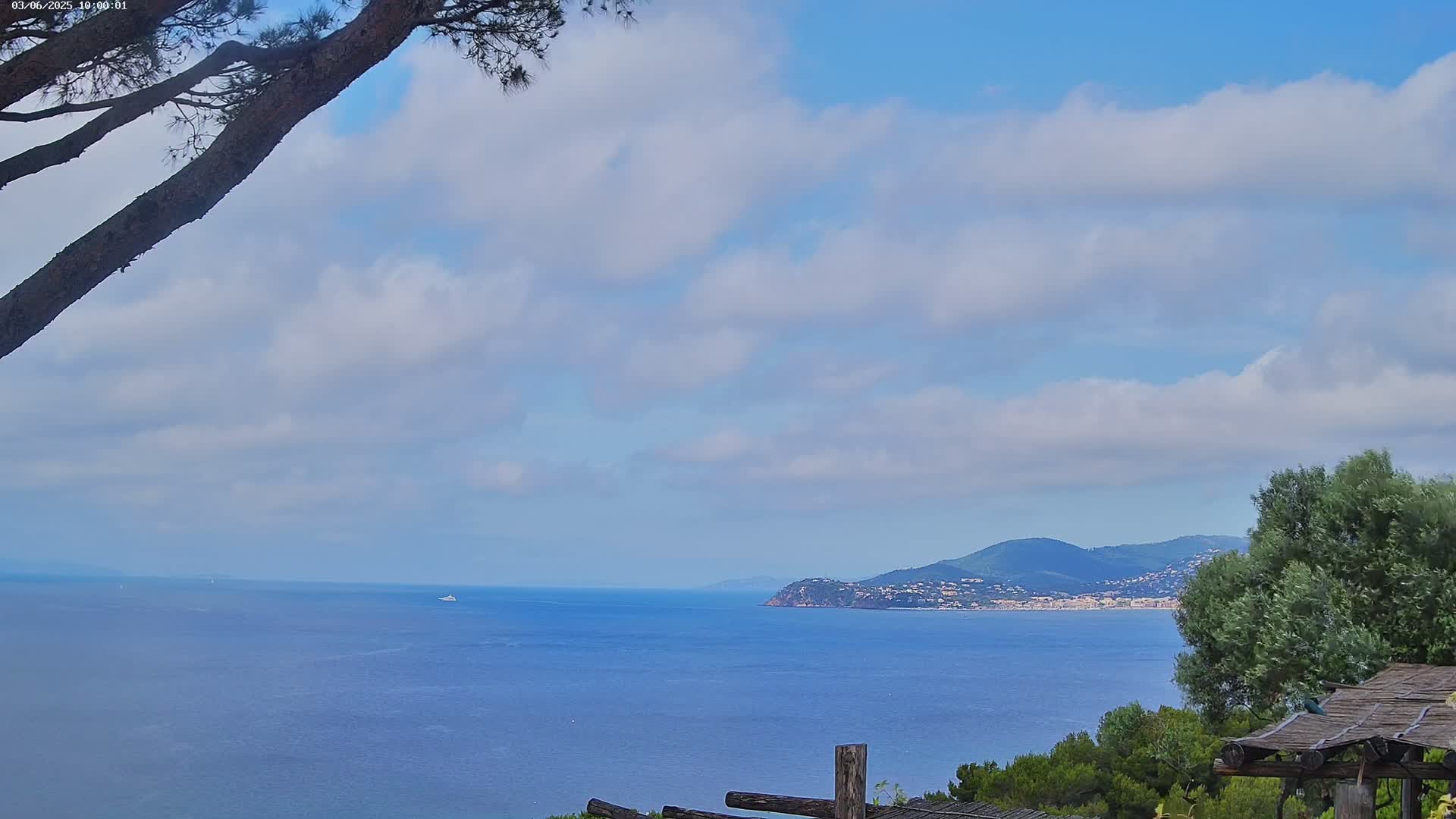 A partly cloudy sky overlooks a calm blue ocean with a distant coastline and hills.