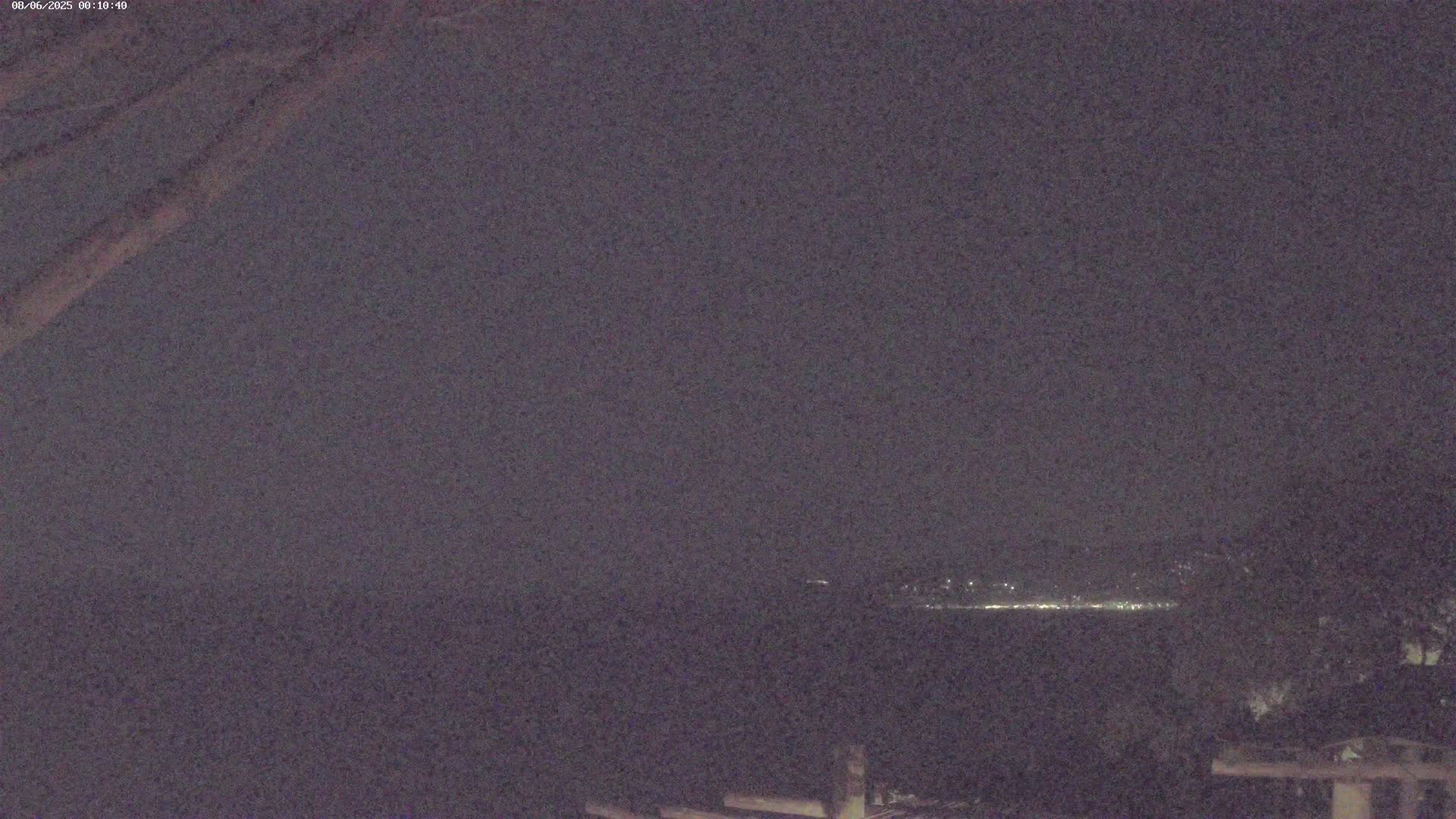 A nighttime long shot shows a distant line of city lights across a dark body of water under a cloudy sky.
