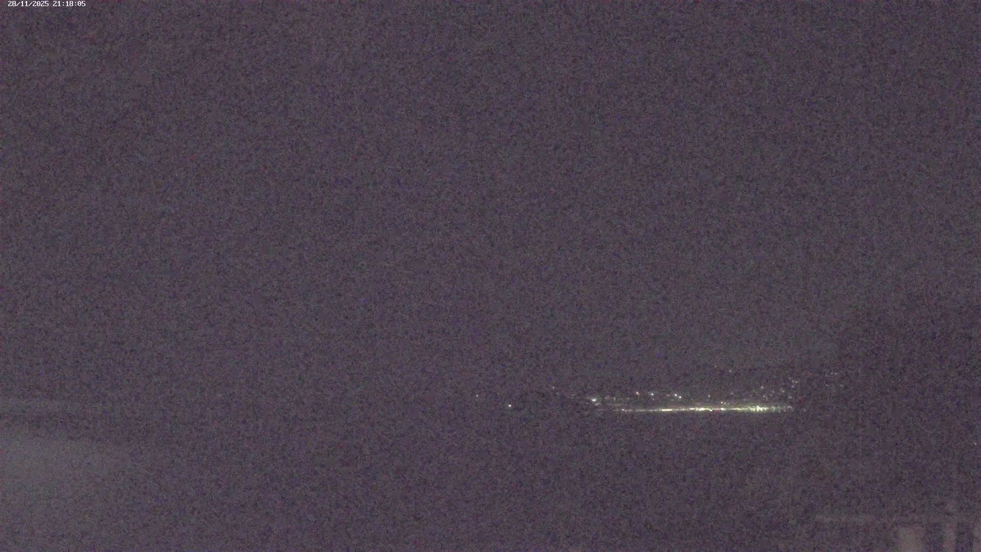 The scene captures a wide, dark expanse at night, with a distant line of diffused city lights visible below an overcast sky.