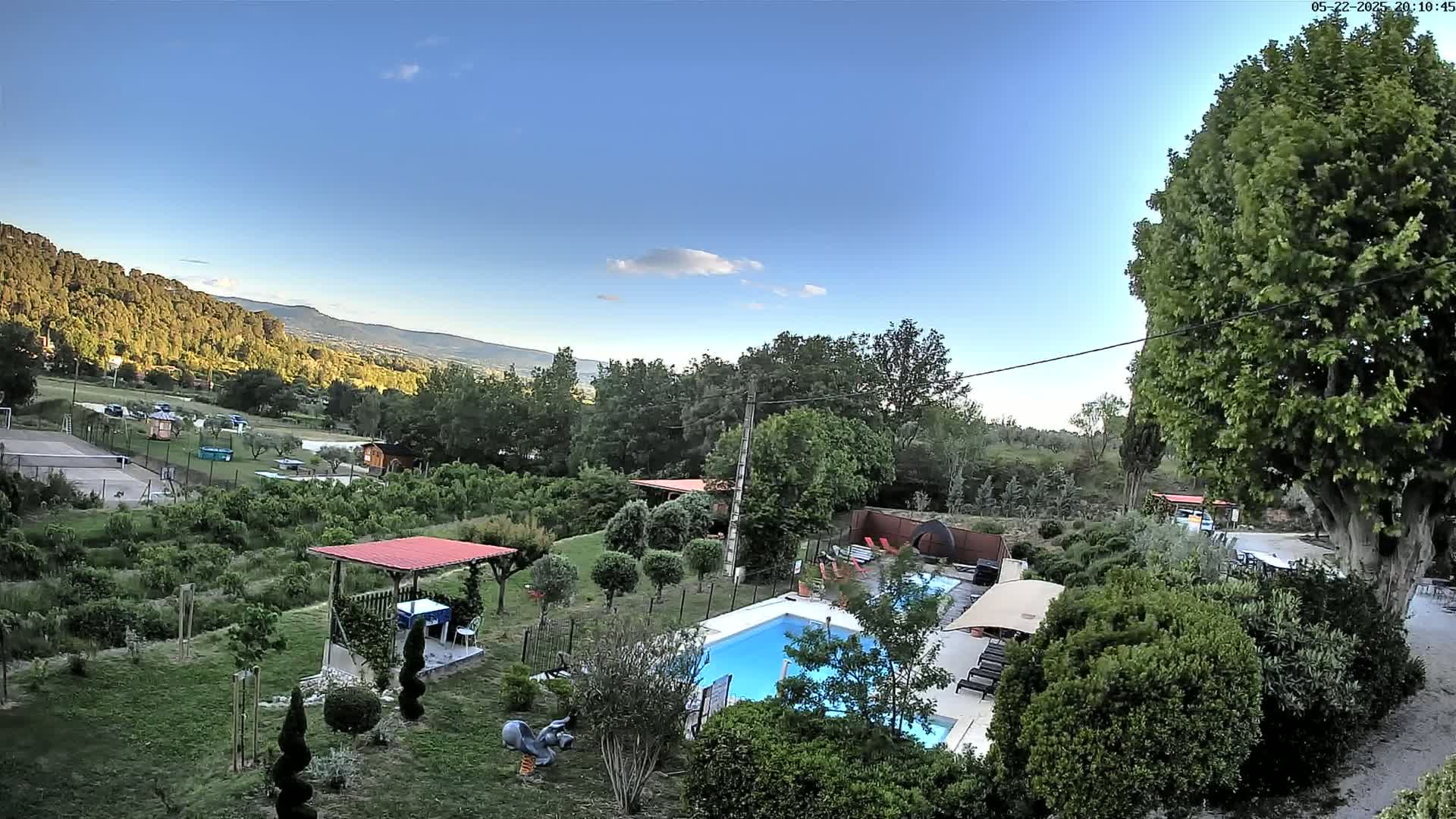 An elevated view shows a swimming pool and surrounding landscaped yard with a pergola, overlooking a valley under a mostly clear blue sky.