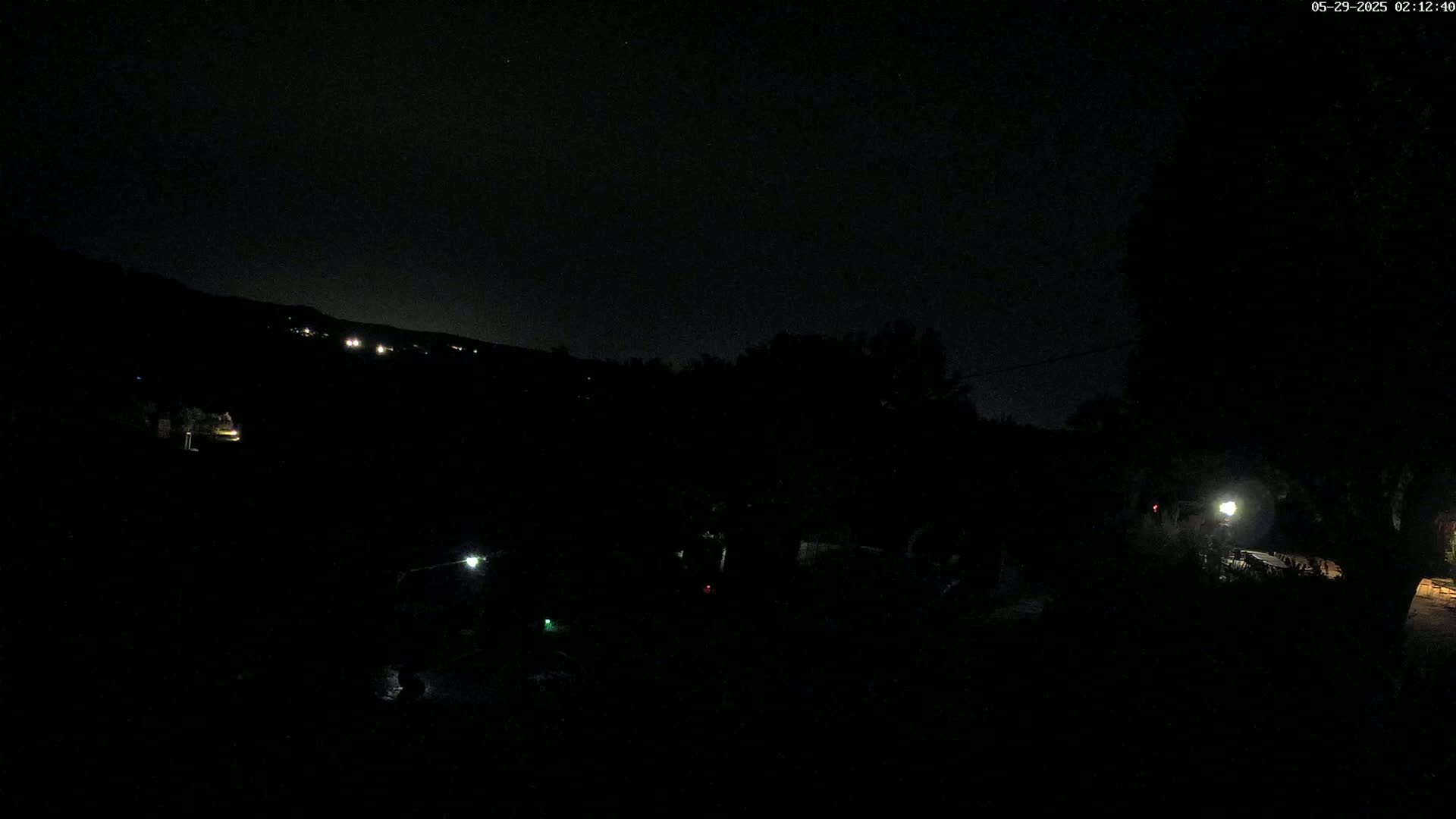 A dark, nighttime scene shows a few faint lights in the distance and closer to the camera, with a mostly clear sky visible.