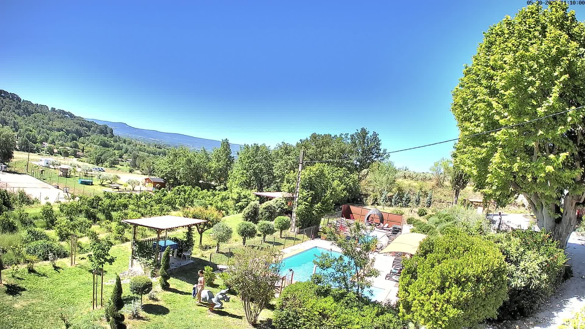 A swimming pool sits in a lush green garden overlooking a valley under a clear blue sky.