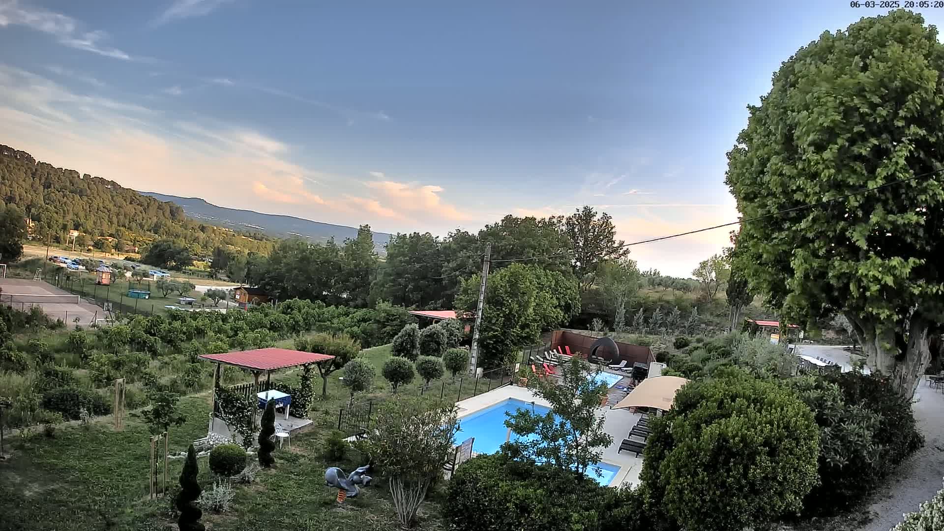 A swimming pool and surrounding garden are situated on a property overlooking a distant mountain range under a partly cloudy, twilight sky.