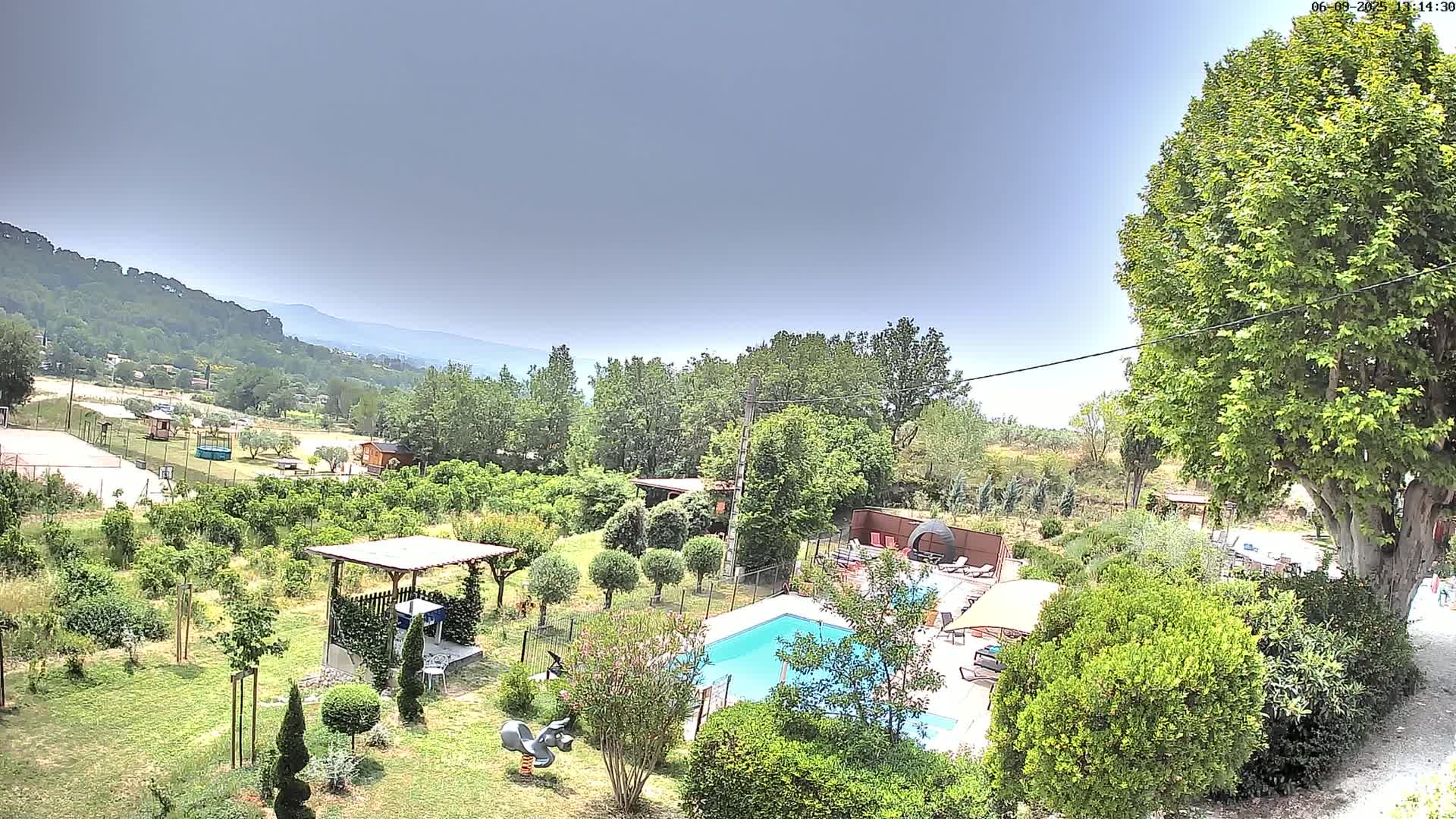 A swimming pool and lush garden are situated on a property overlooking a valley under a mostly clear sky.