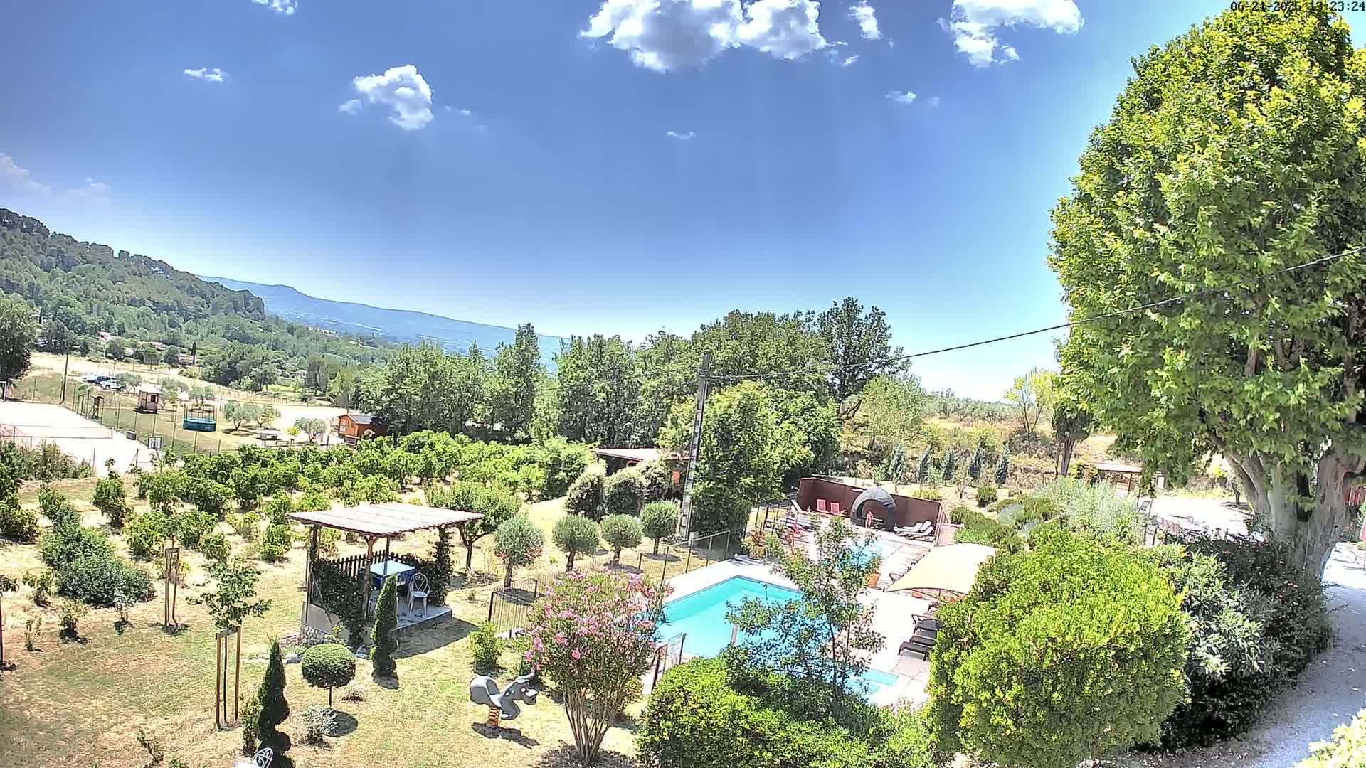 A swimming pool sits in a sunny, landscaped yard with a view of distant mountains under a mostly clear blue sky.
