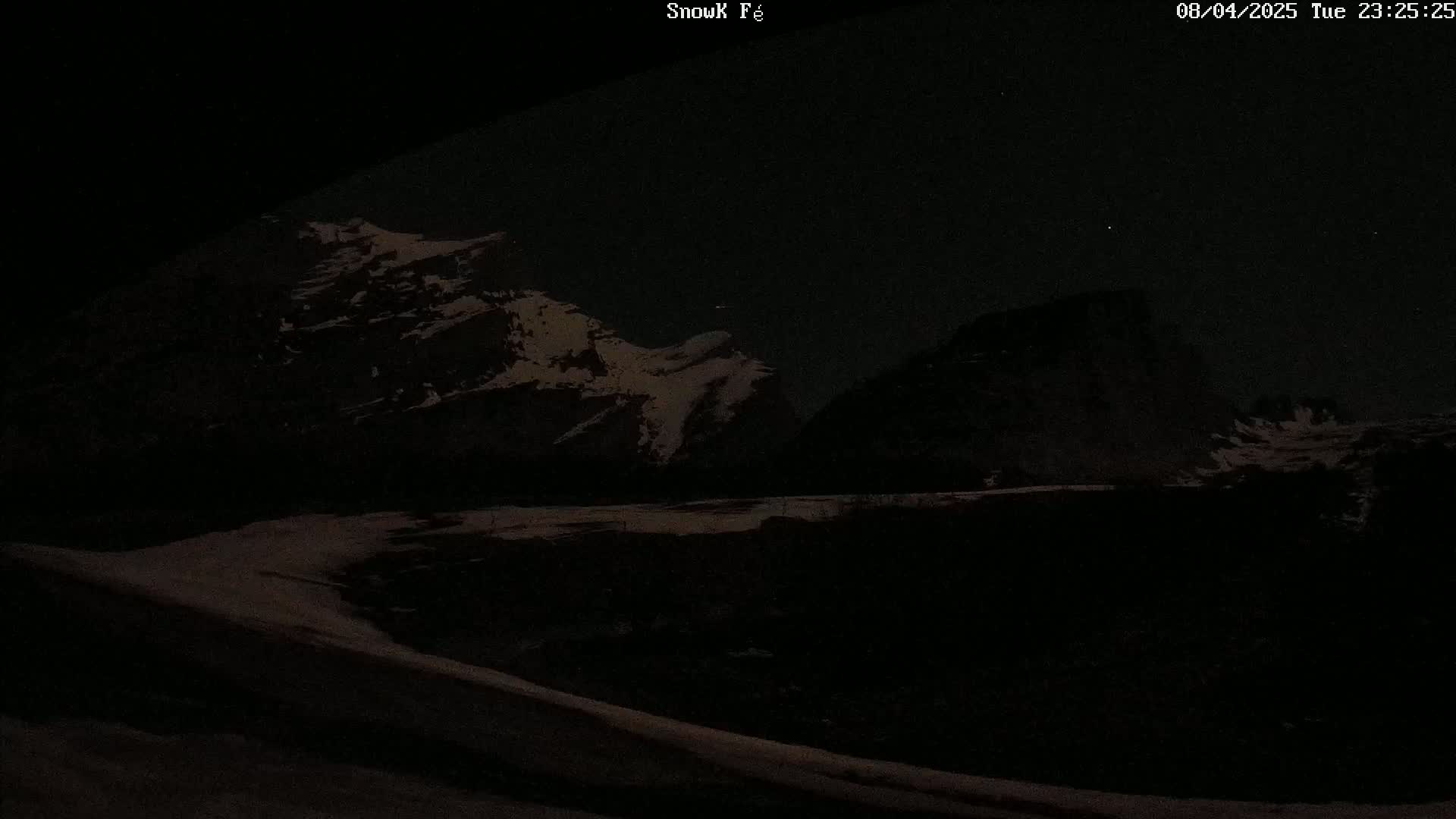 A nighttime view of snow-covered mountains under a dark, starry sky.