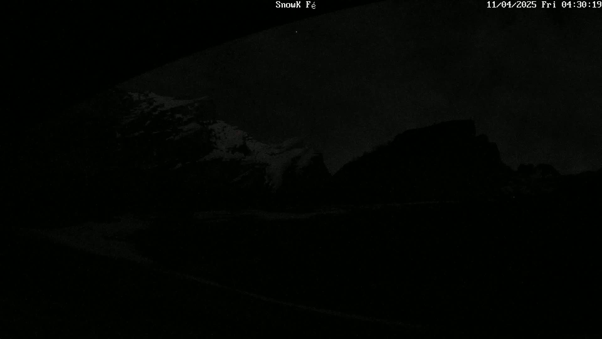 A dark, nighttime view of snow-capped mountains under a mostly clear sky.