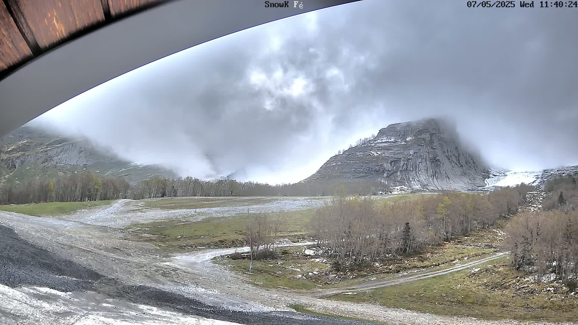 A cloudy mountain landscape with patchy snow and leafless trees, viewed from under an awning.