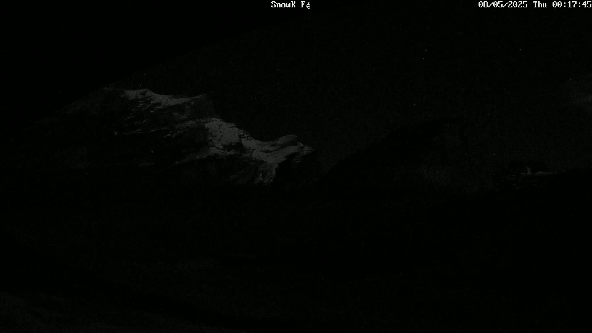 A nighttime, low-light image shows snow-covered mountains under a clear, starry sky.