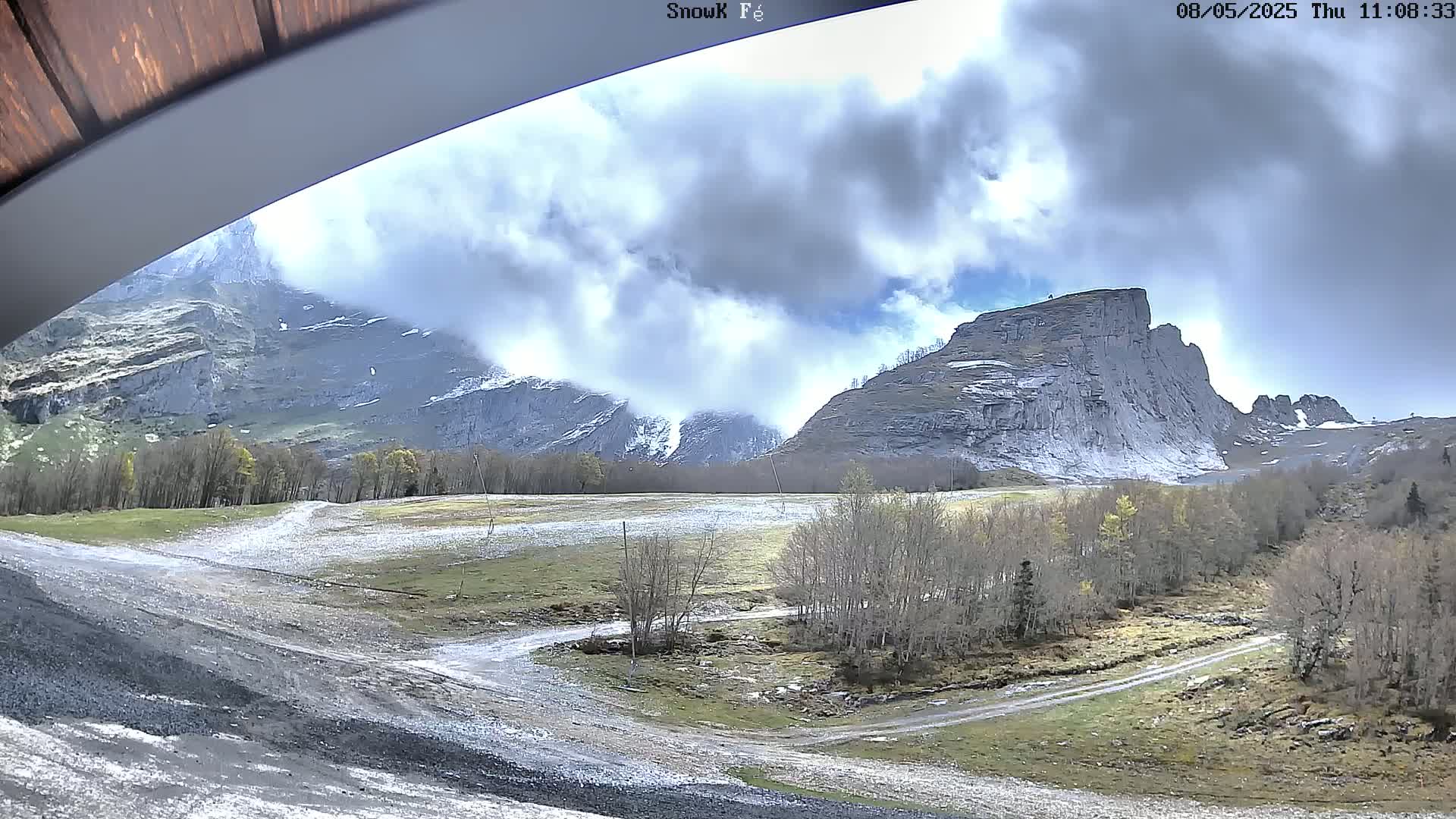 A cloudy day reveals a mountainous landscape with a large, prominent rock formation, sparsely wooded areas, and a gravel road winding through the scene.