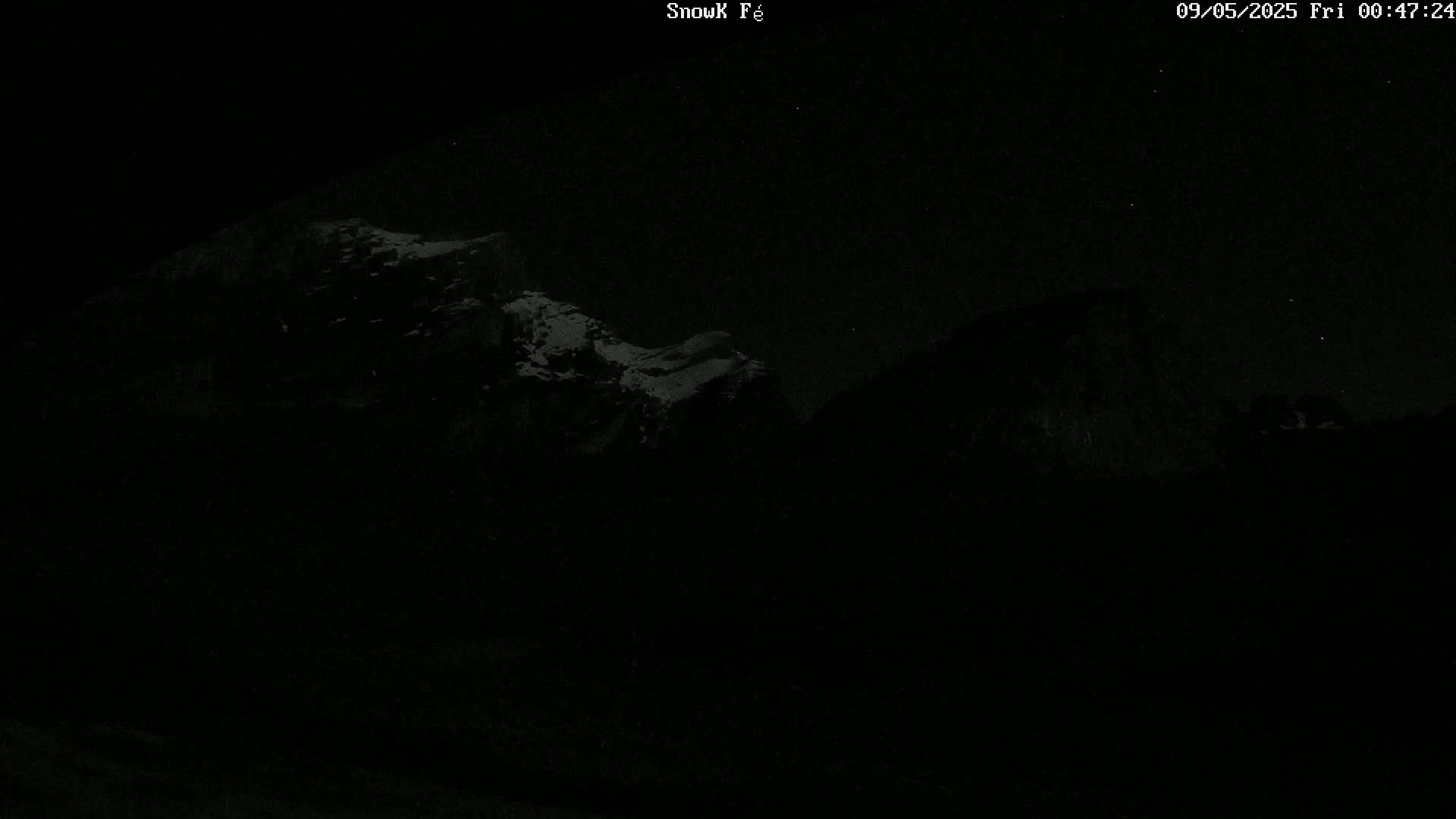 A nighttime, low-light view shows snow-capped mountains under a clear, starry sky.