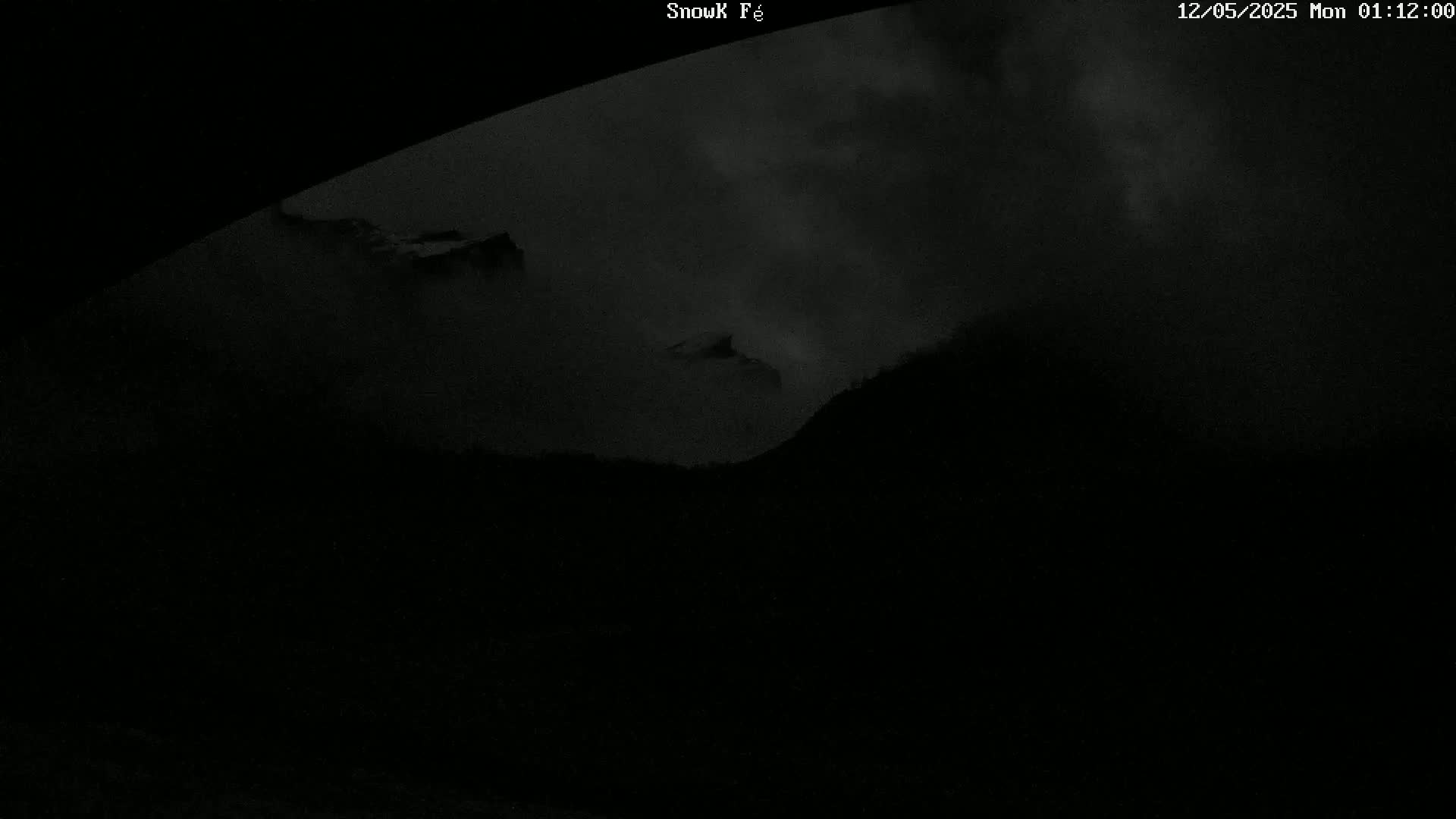 A dark, cloudy night scene shows silhouetted mountains partially obscured by fog or low clouds.