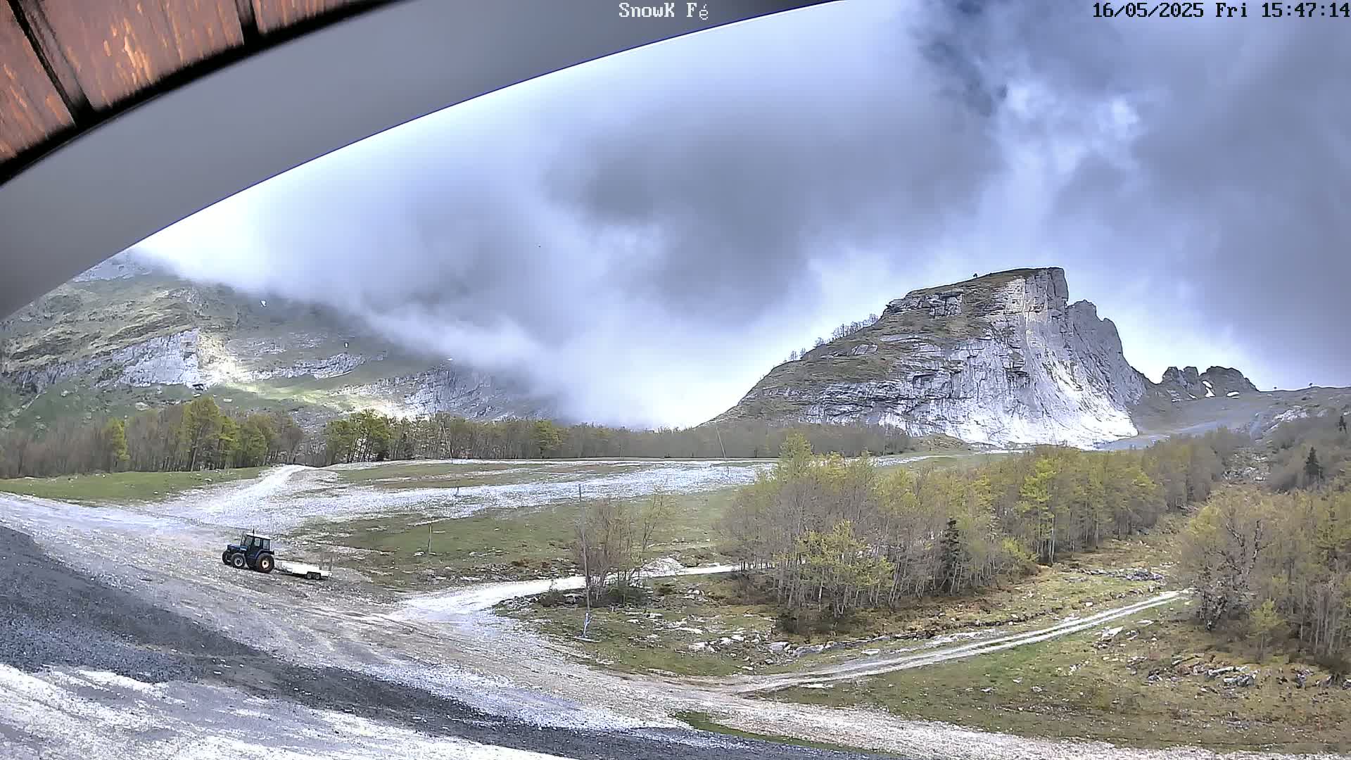 A tractor pulls a trailer on a gravel road in a mountainous area under a cloudy sky.