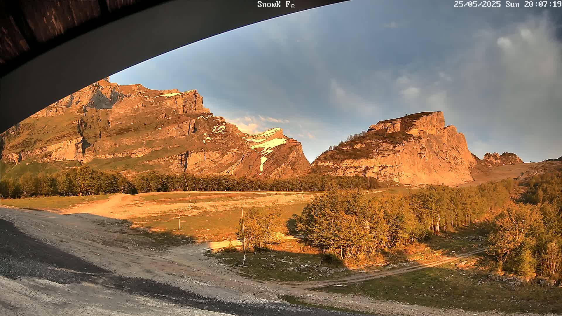 Large, rocky mountains bathed in the golden light of sunset are partially visible from under an overhang, with a sparsely wooded valley in the foreground.