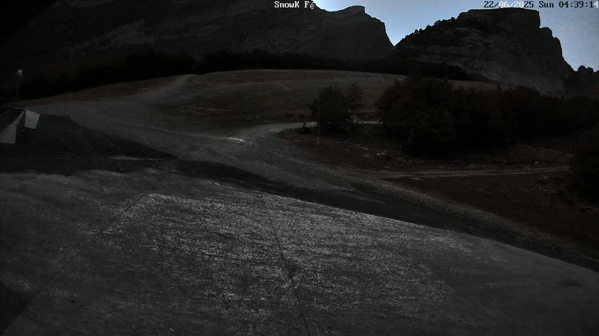 A dark, mostly dirt road winds through a sparsely vegetated landscape under a twilight sky, with a large rock formation looming in the background.