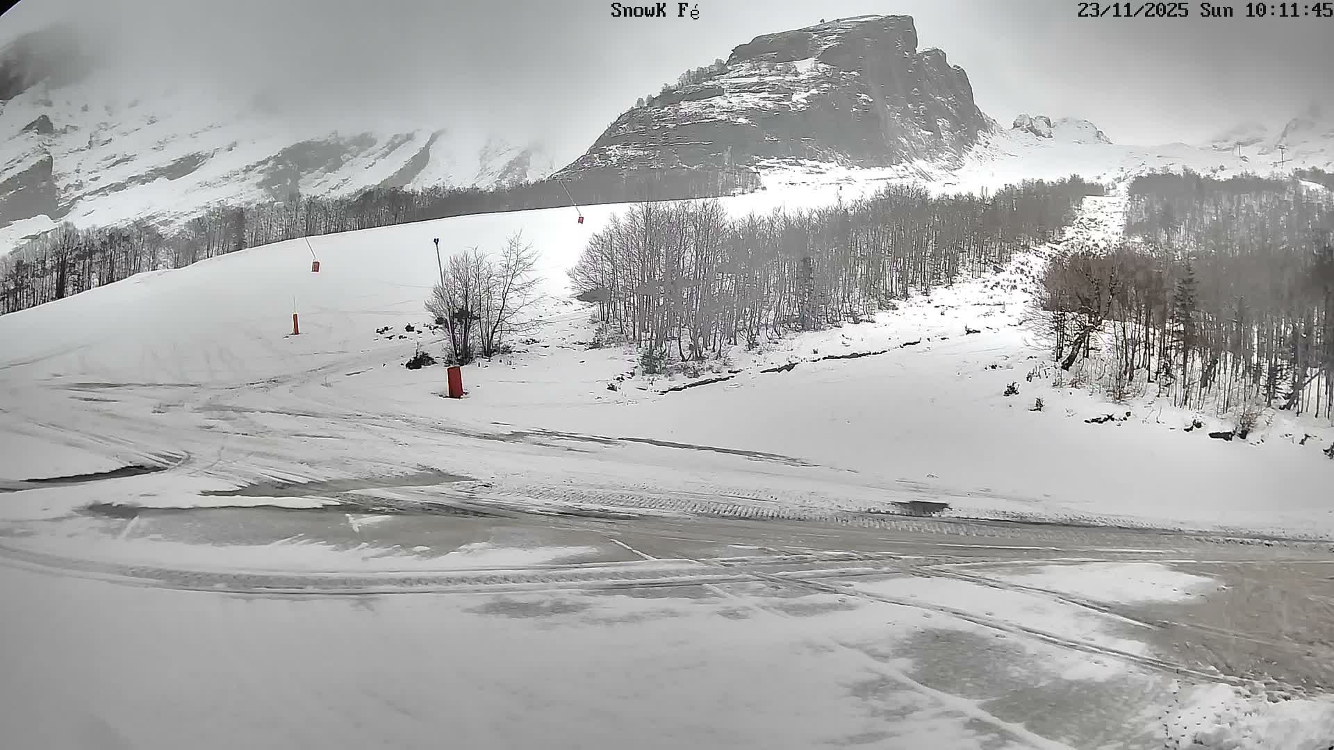 A snow-covered mountain landscape with bare trees, visible ski lift pylons, and a slushy foreground path is presented under an overcast sky.