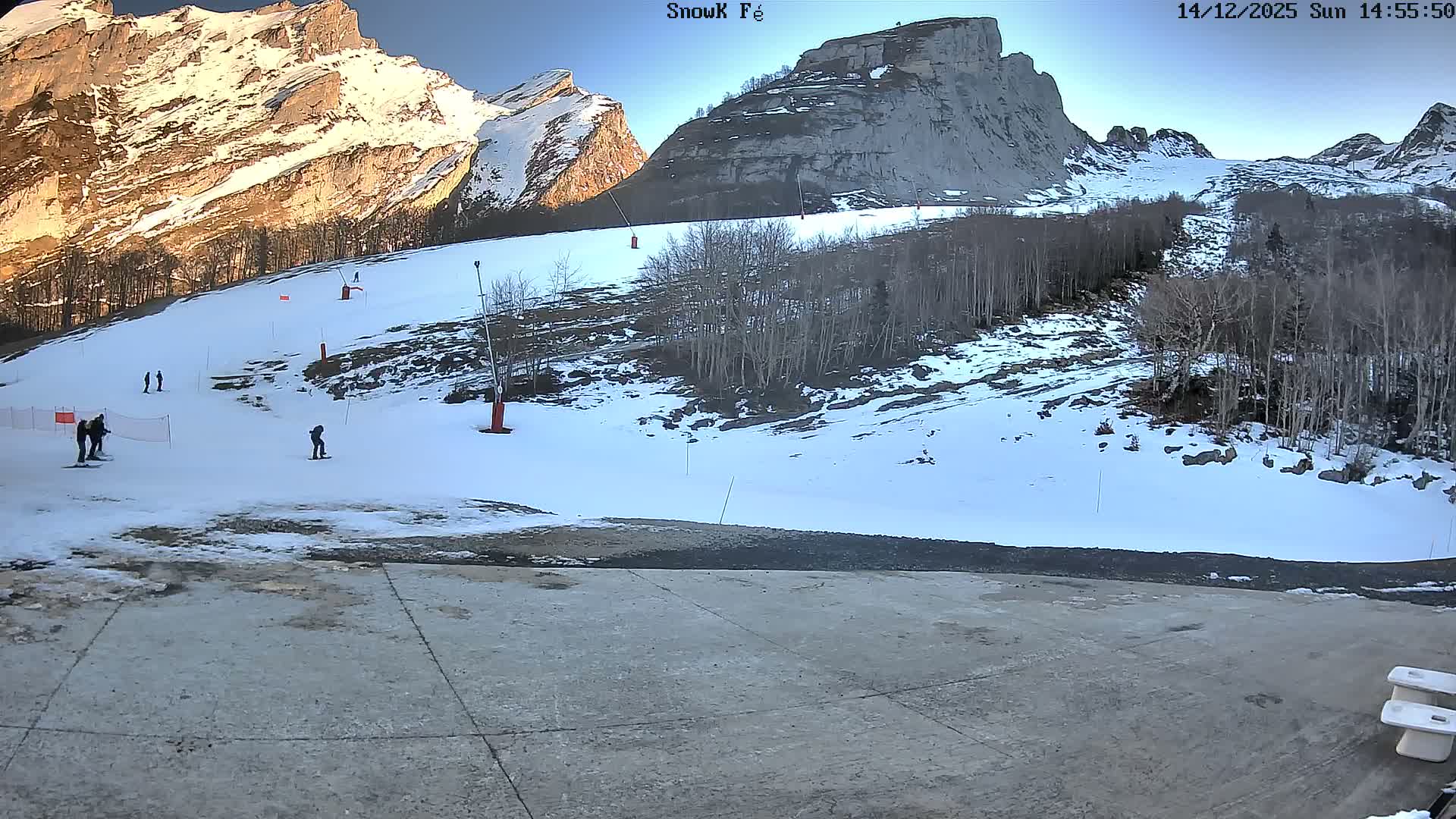 A snow-covered mountain landscape with bare trees, visible ski lift pylons, and a slushy foreground path is presented under an overcast sky.