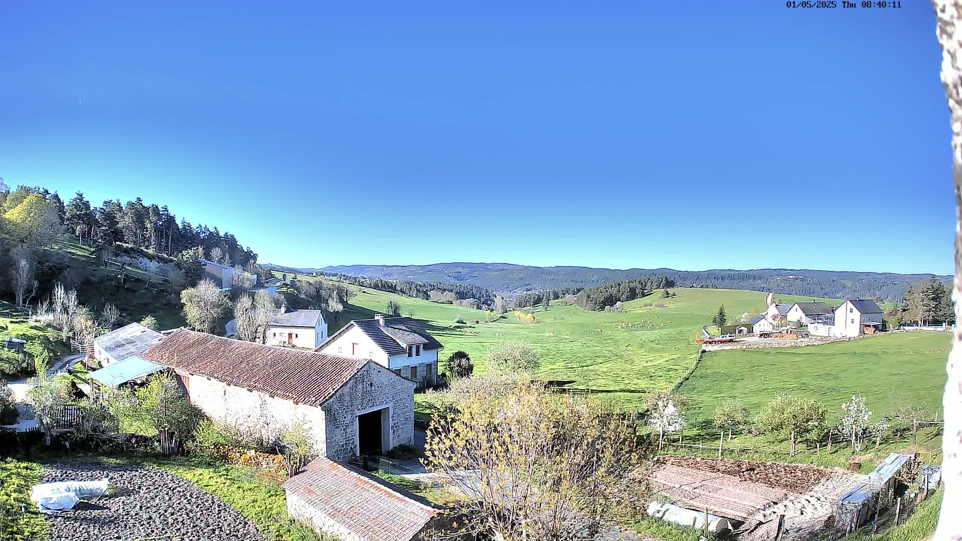 A sprawling green valley dotted with farmhouses and stone barns under a clear blue sky.