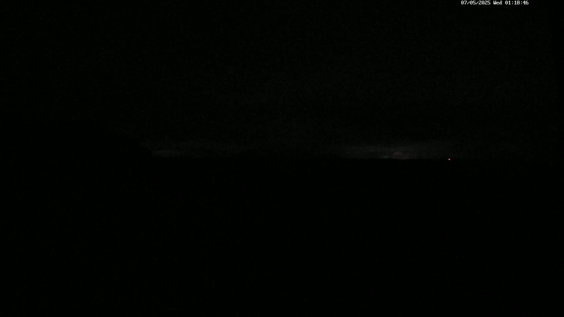 A dark, nighttime scene shows a faint, light horizon with a single, small red light visible in the distance.