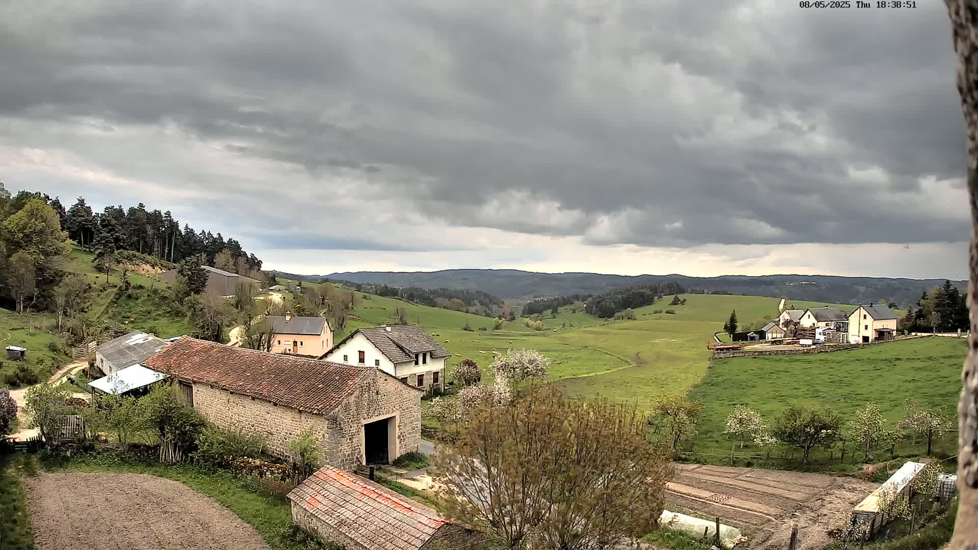 Stone farm buildings and houses sit on rolling green hills under a cloudy sky.