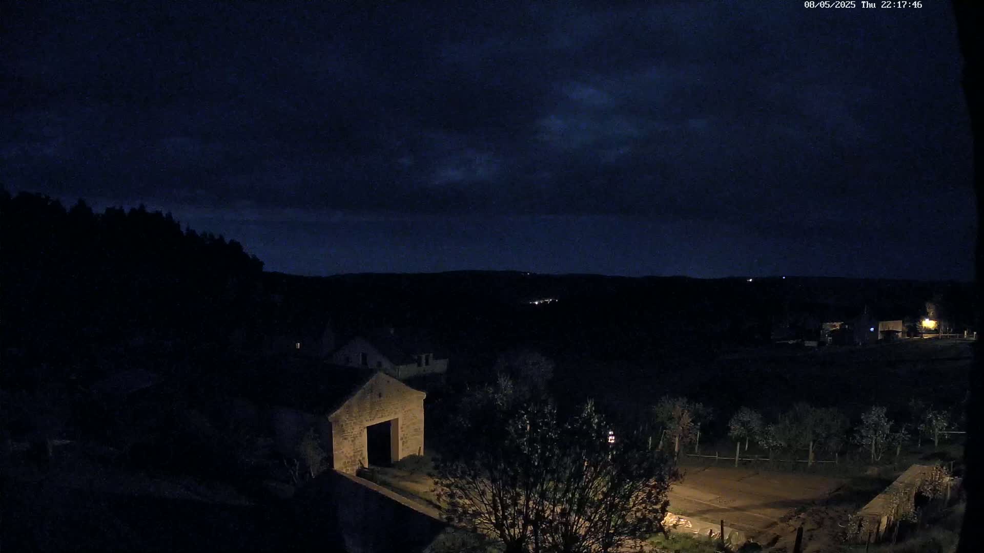 A stone barn and other buildings are visible under a dark, cloudy night sky.