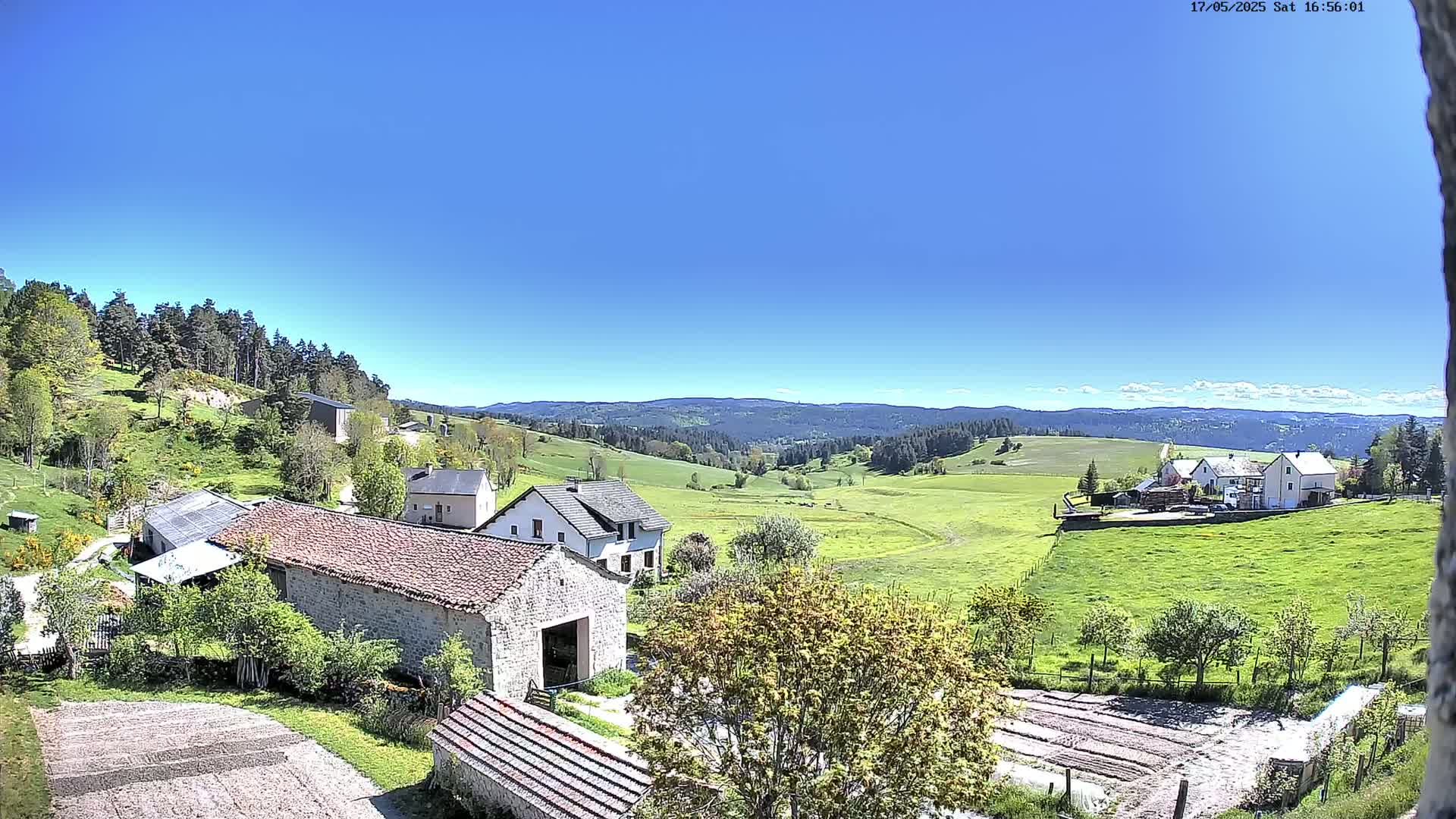 Stone farm buildings sit on a hillside overlooking a verdant valley under a clear blue sky.