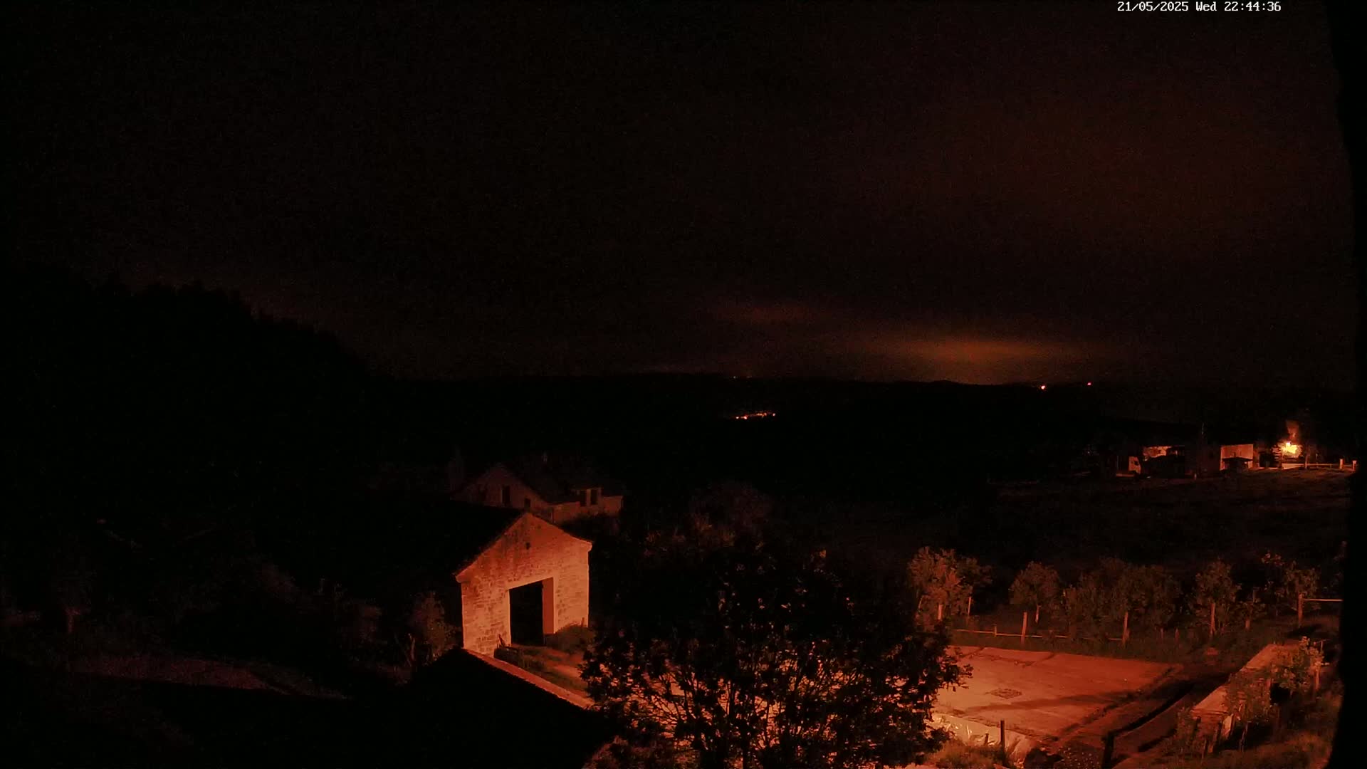 A nighttime view of a stone building and surrounding area under a dark, reddish sky.