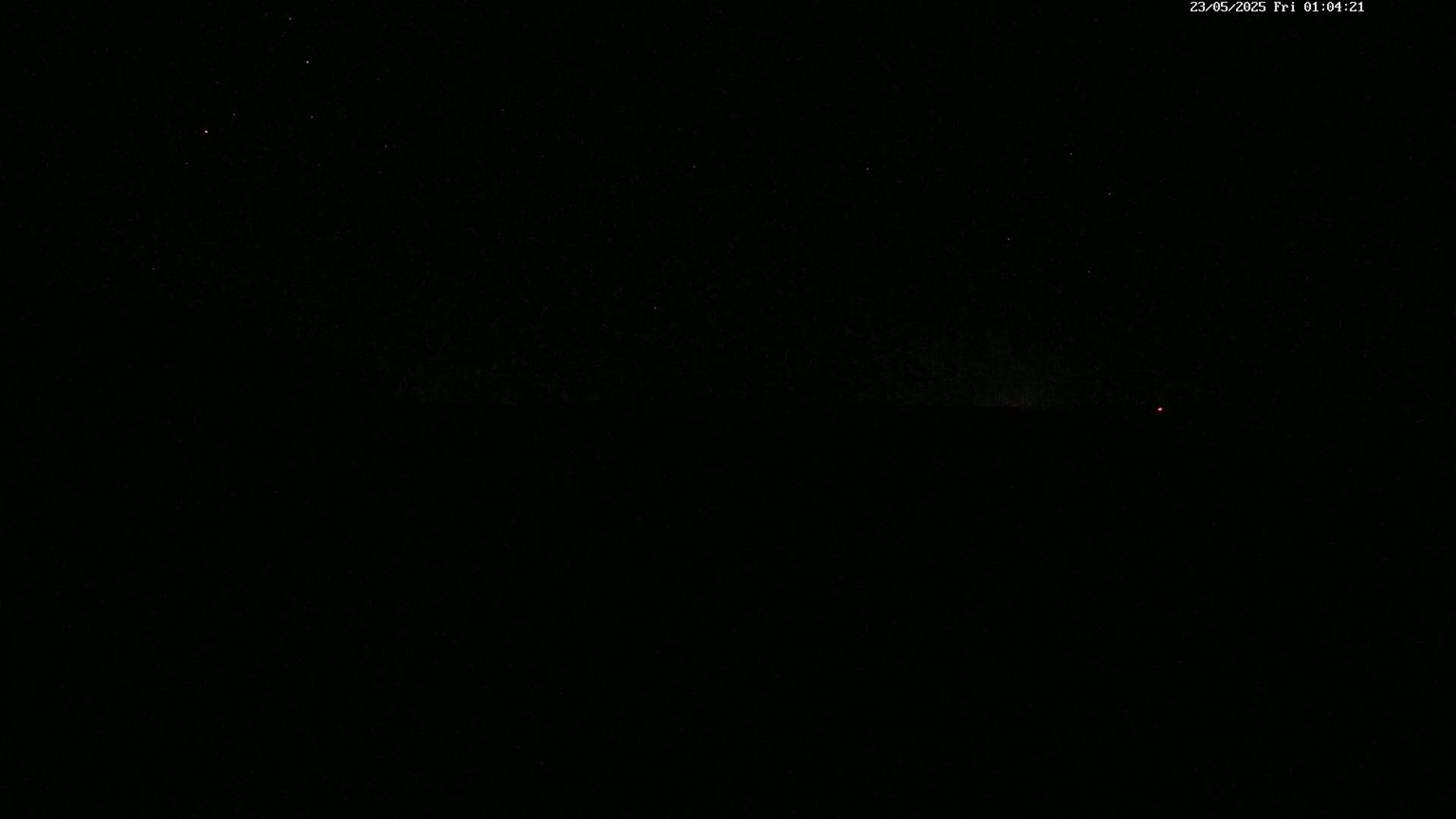 A dark night sky with a few visible stars and a distant red light on the horizon.
