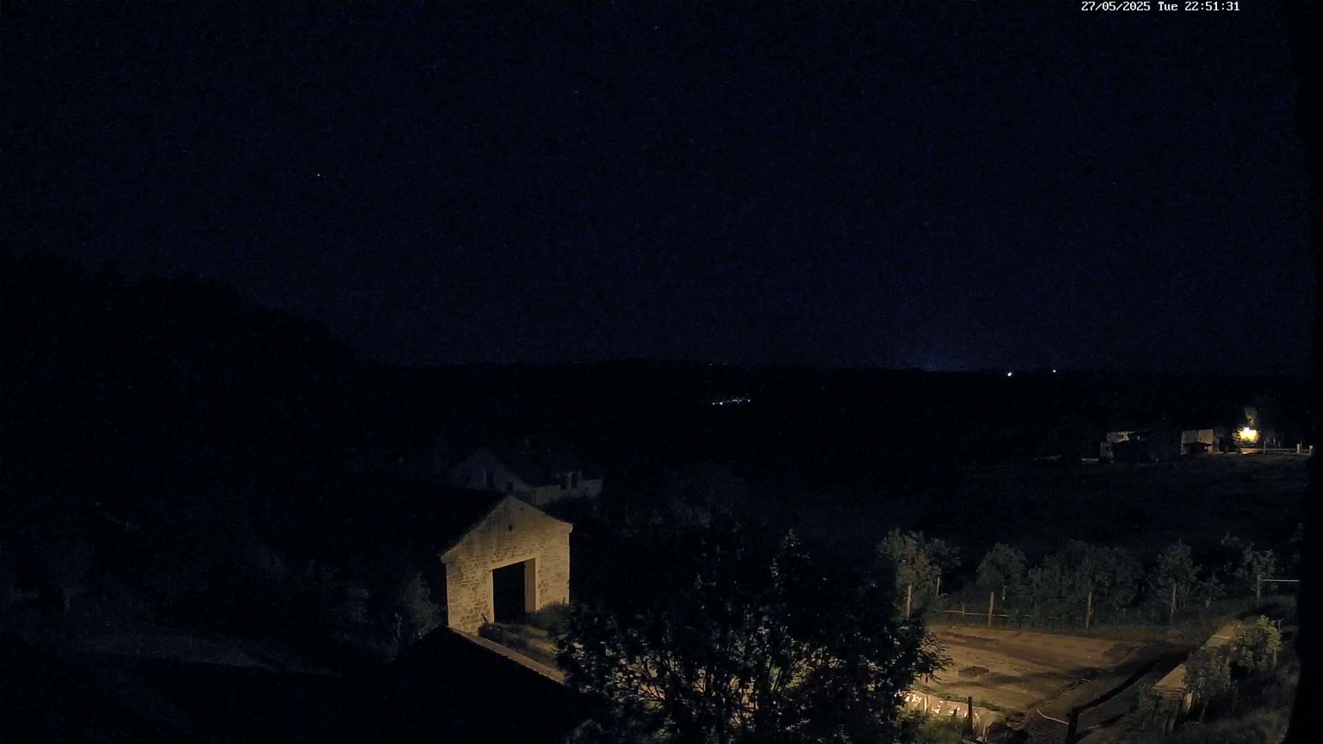A nighttime, dark view of a stone building and surrounding landscape under a clear, starry sky.